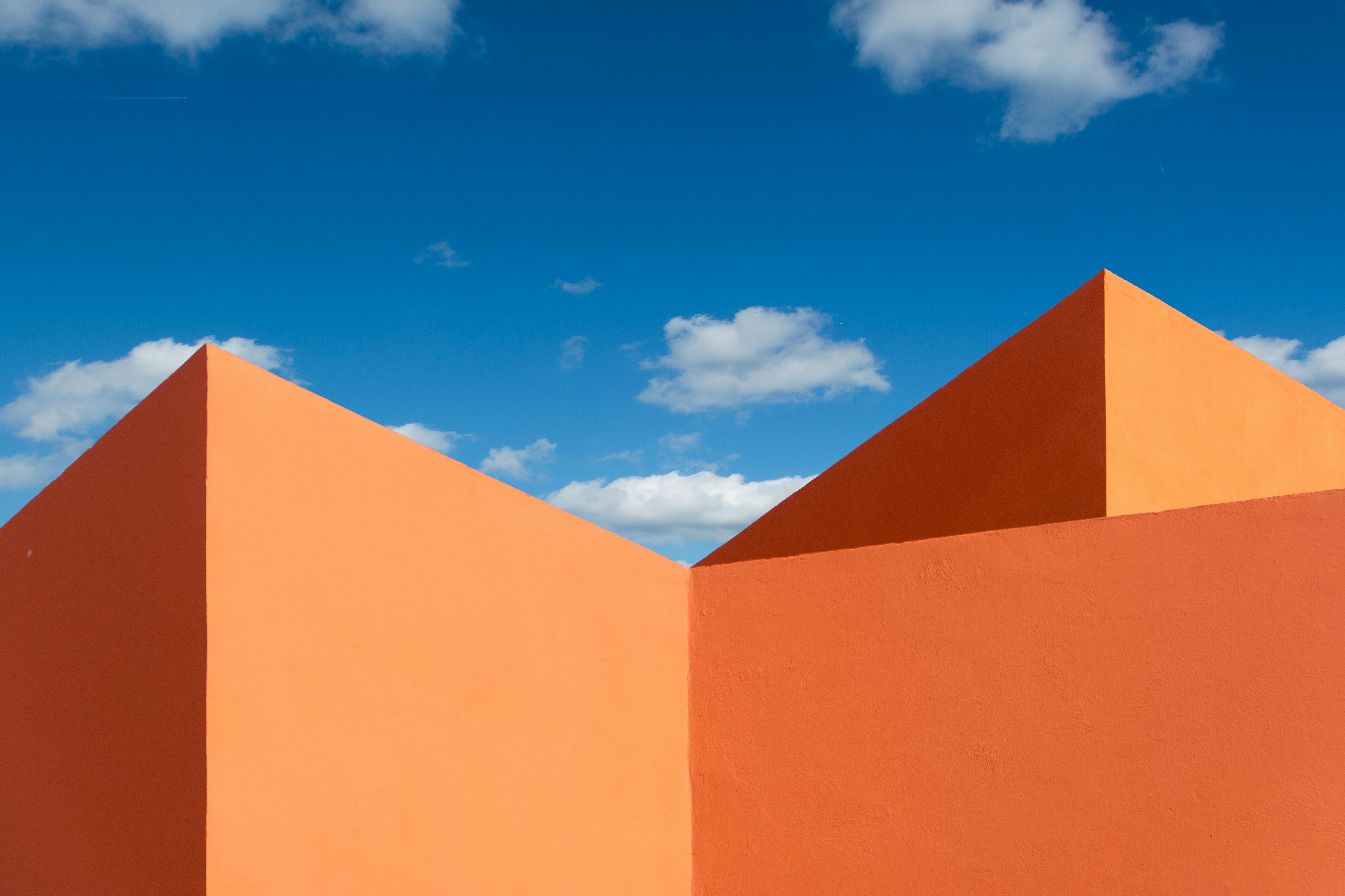 Bright ocher structure with geometric shapes set against a vibrant blue sky with clouds.
