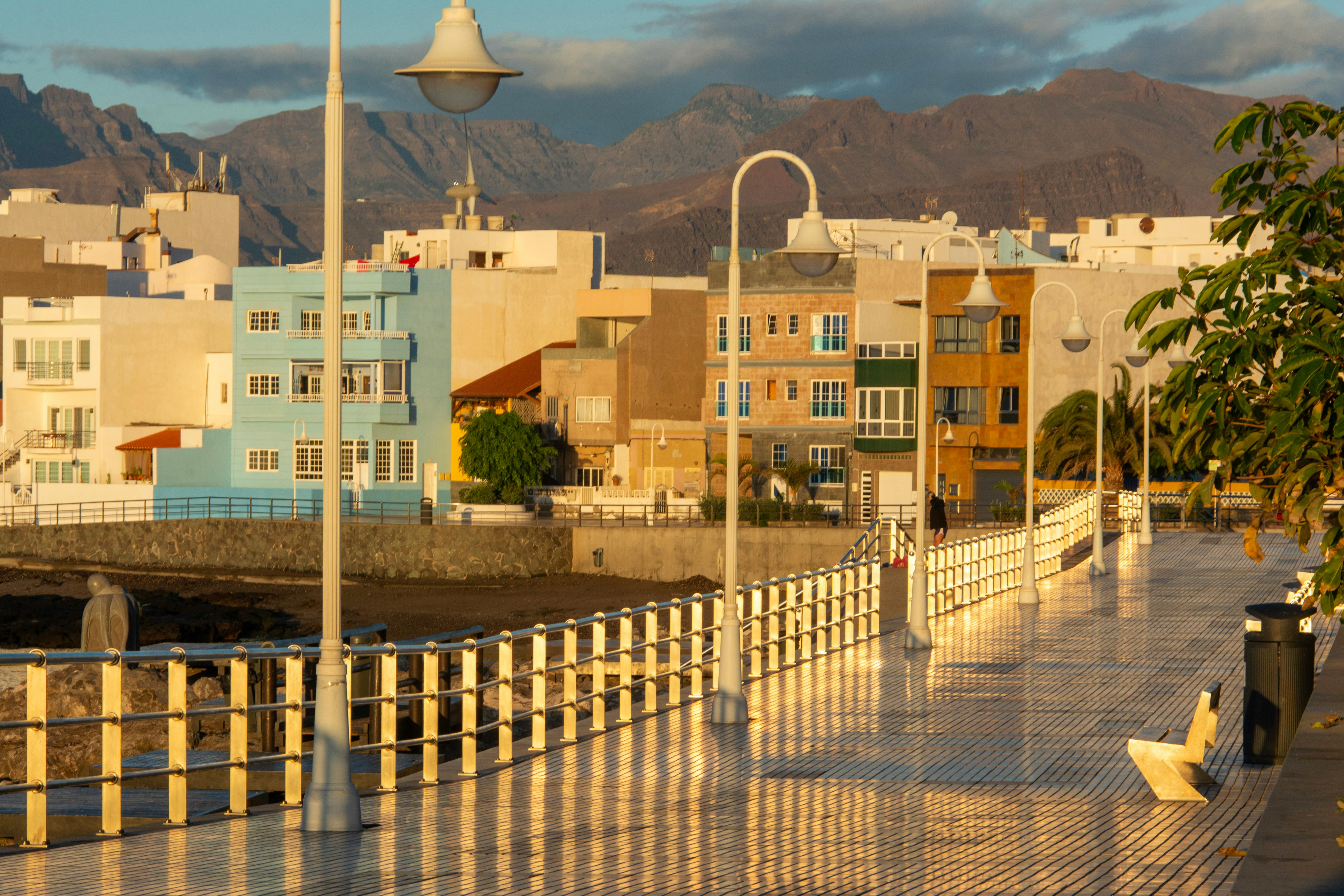 A picturesque promenade in Arinaga, Spain, with colorful buildings and mountain backdrop at sunrise.