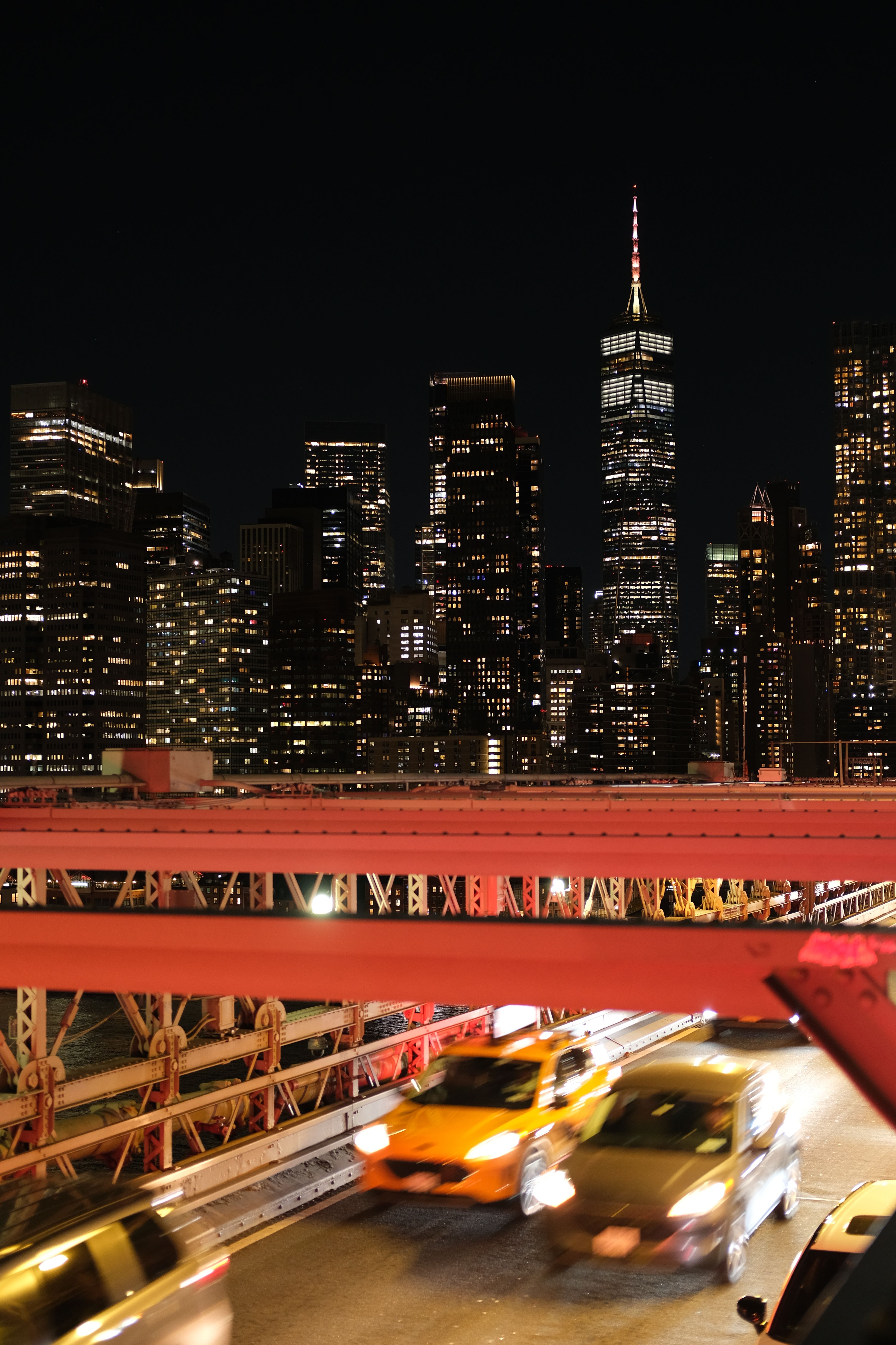 Long exposure of traffic on the Brooklyn Bridge with New York City skyline at night.