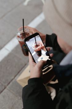 A person captures an iced coffee using a smartphone camera outdoors.