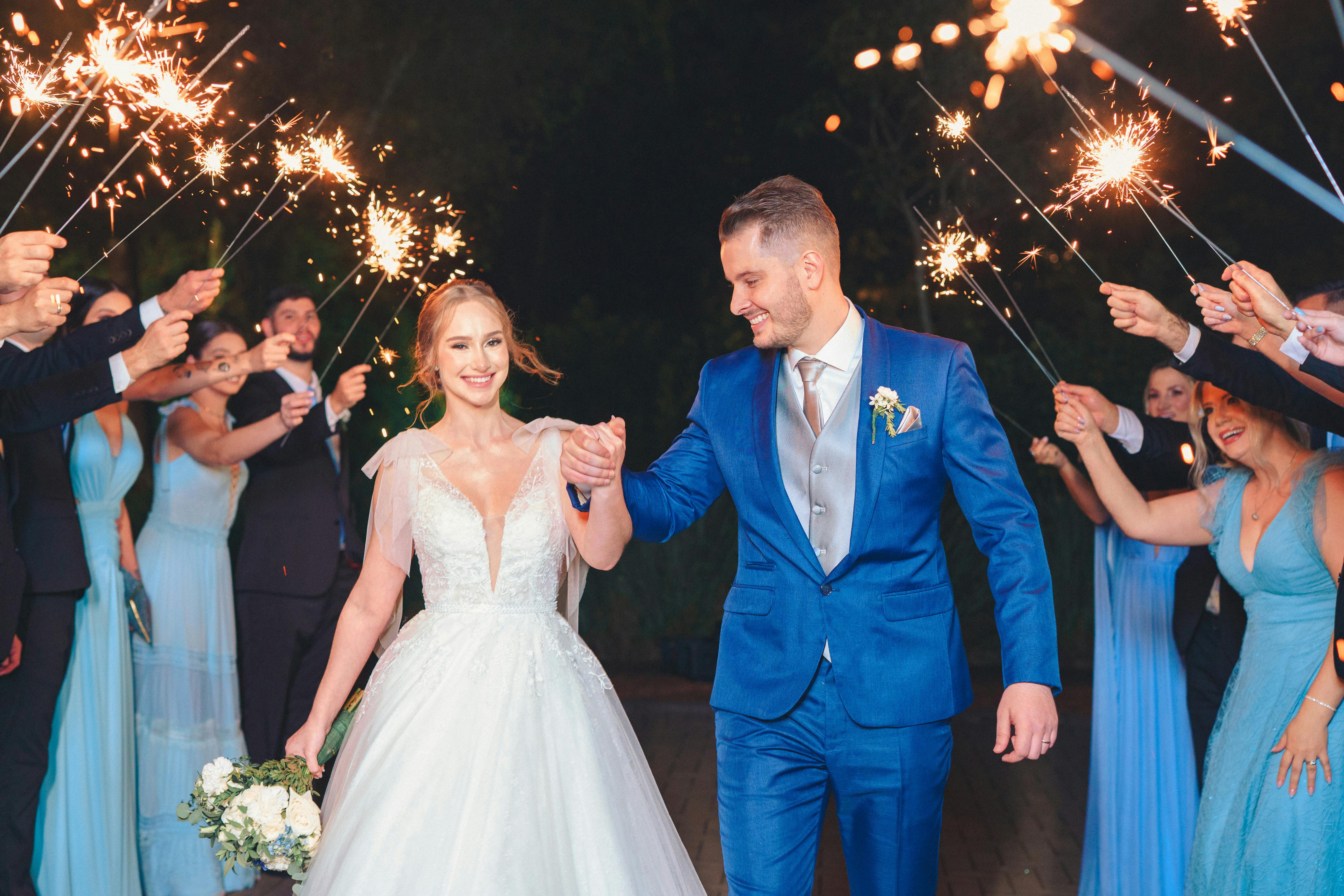 Joyful bride and groom walking amid sparkler celebration at night wedding event.