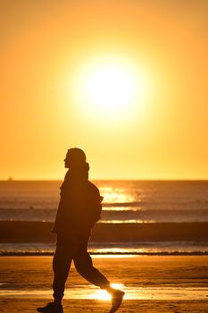 A person walking along the beach at sunset with a beautiful orange sky.