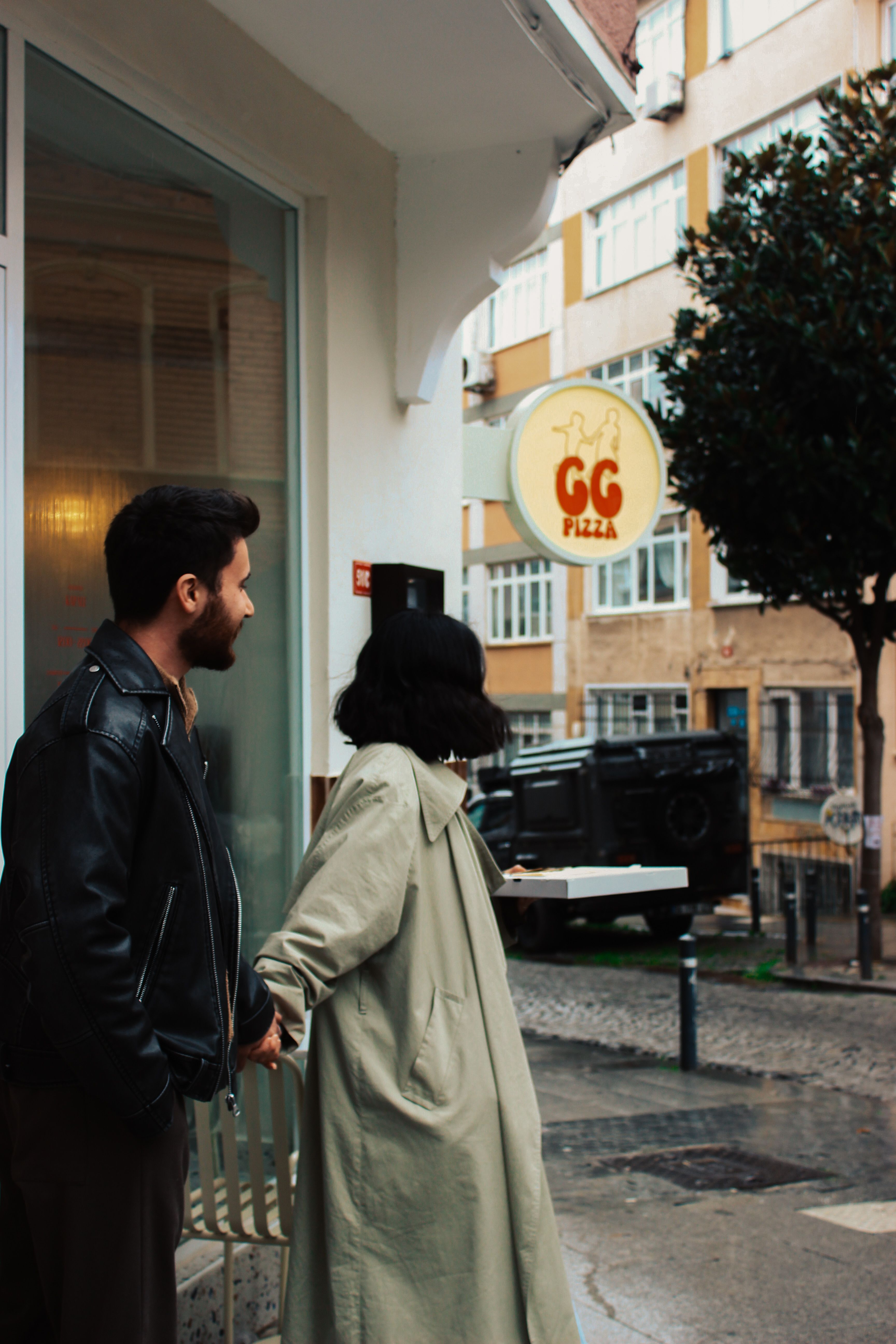 A couple standing outside a pizza shop on a rainy street.