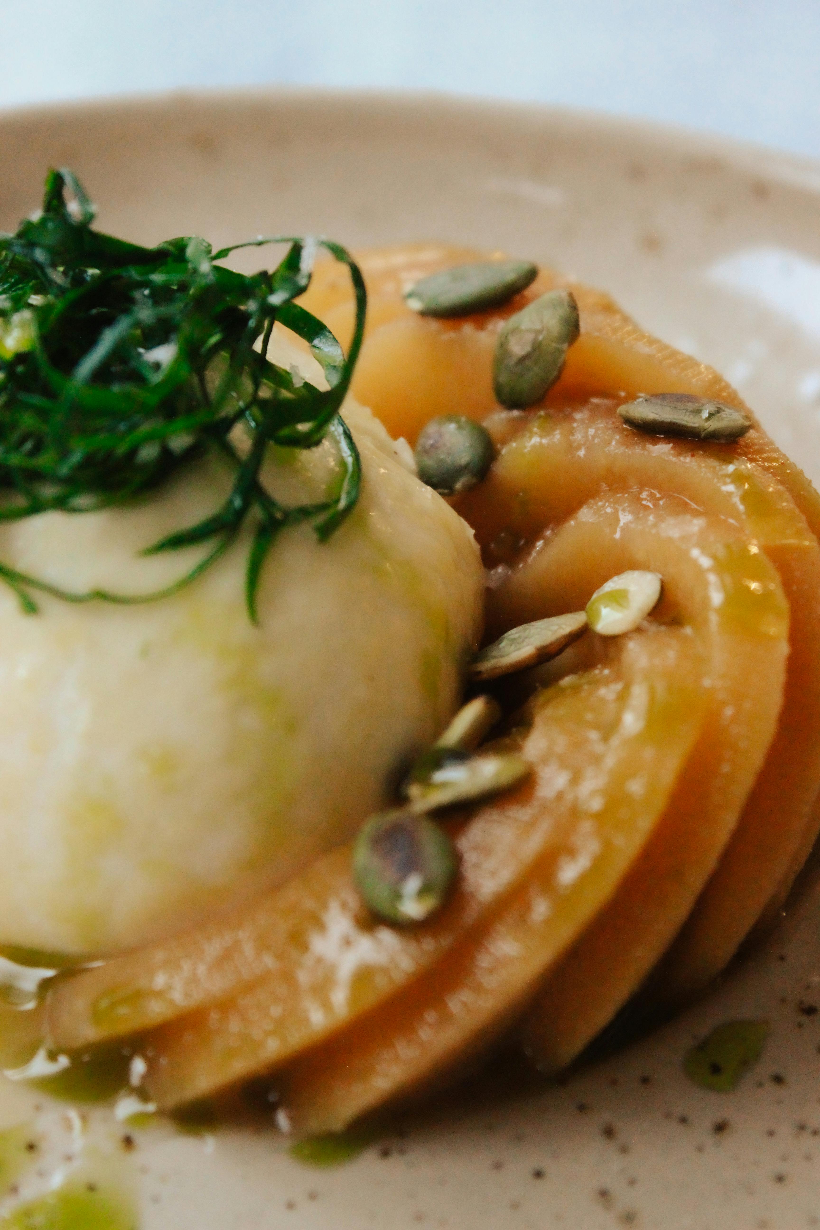 Elegant presentation of a dish with cream, pumpkin seeds, and herbs on a speckled plate.