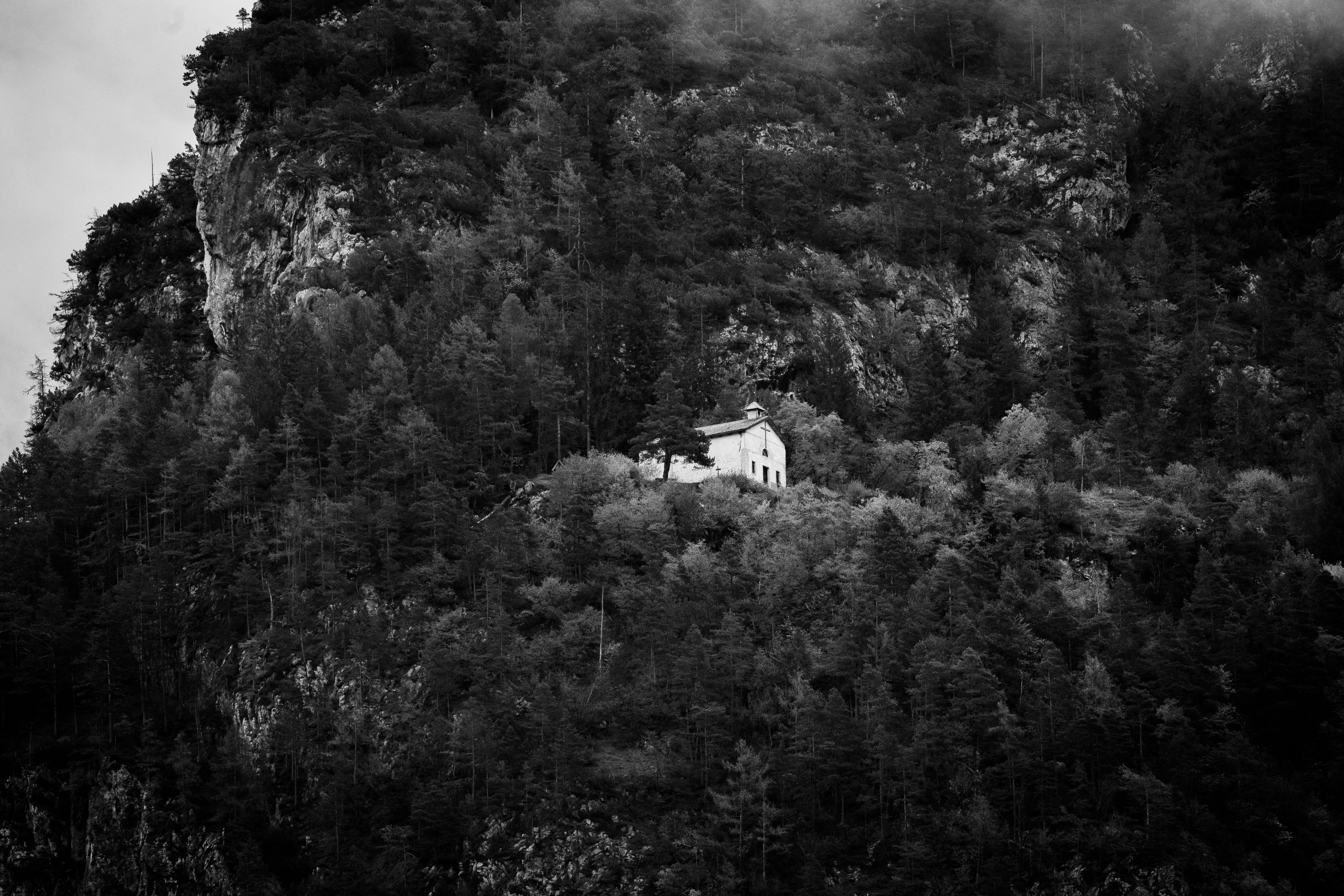A solitary cabin nestled in a rugged mountain landscape surrounded by dense forest.