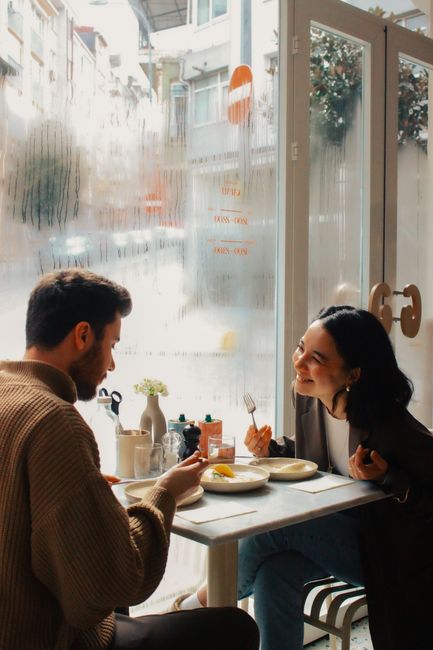Two adults enjoying a meal in a cozy cafe, laughing and bonding by the window.