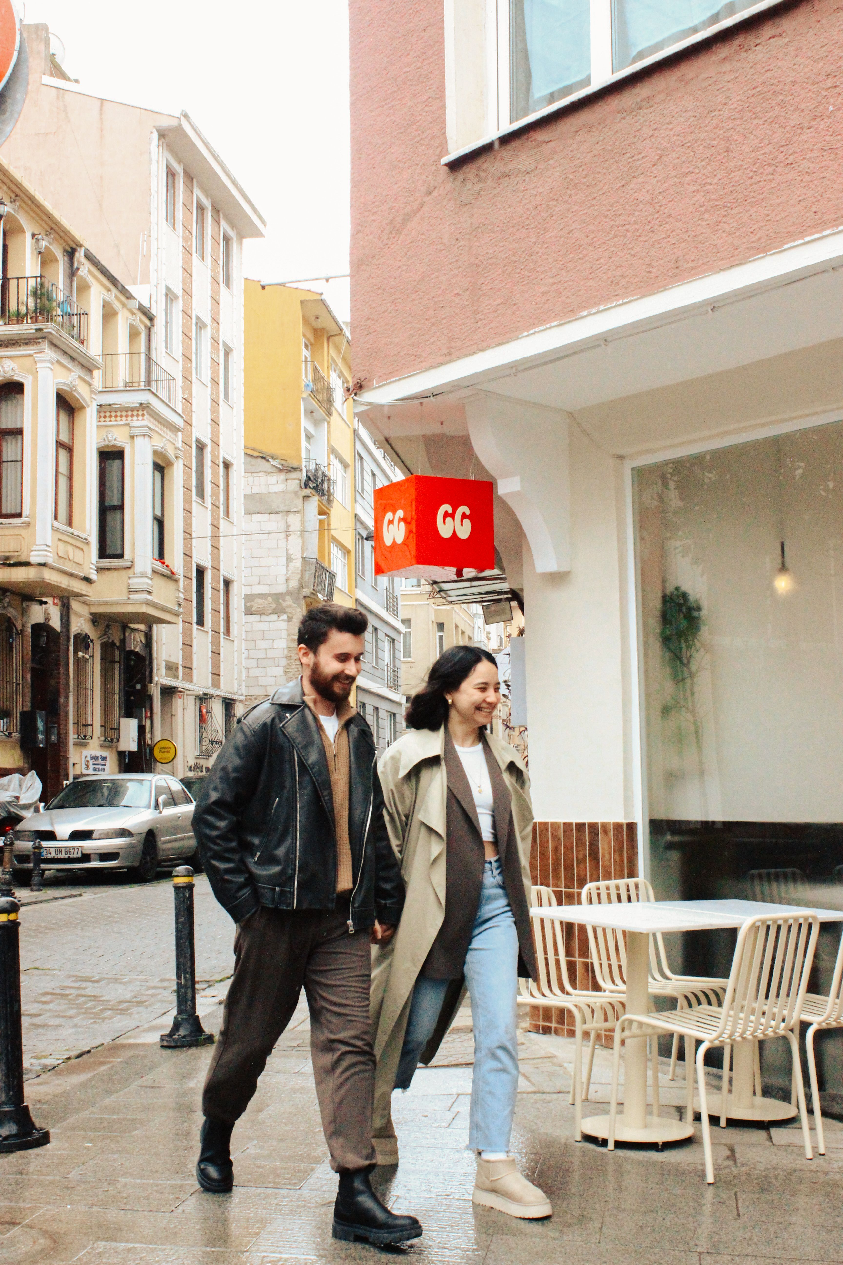 A fashionable couple walks past a European cafe in an urban street on a cloudy day.