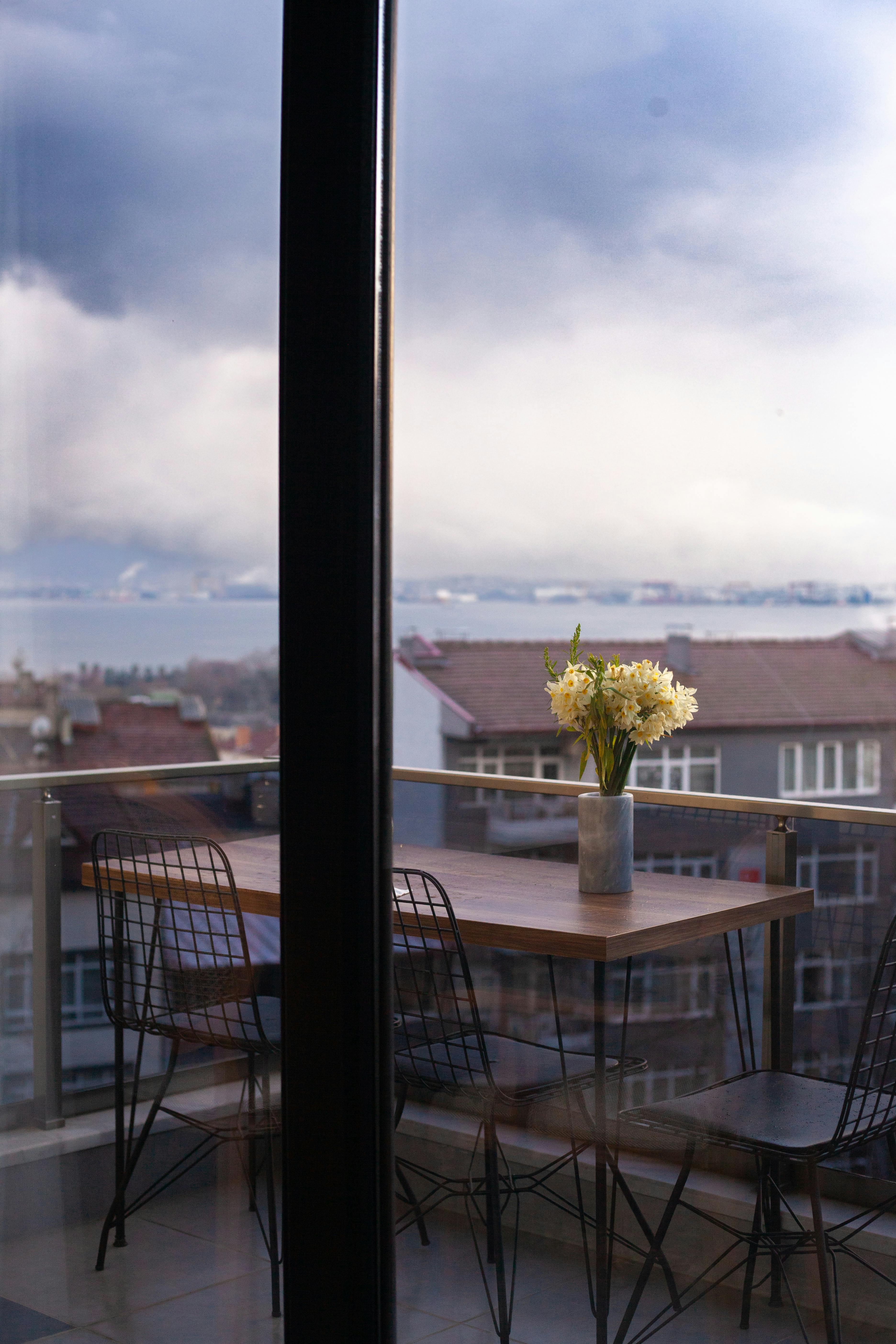 Stylish balcony with a vase of flowers overlooking a sea and city view, perfect for urban relaxation.