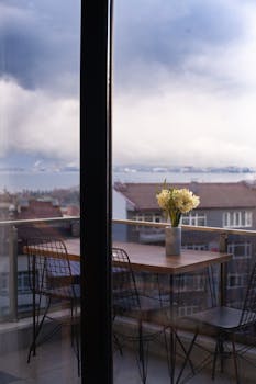 Stylish balcony with a vase of flowers overlooking a sea and city view, perfect for urban relaxation.