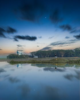 Tranquil scene of a lone figure beside a calm reflection of sky and trees in Bangladesh.