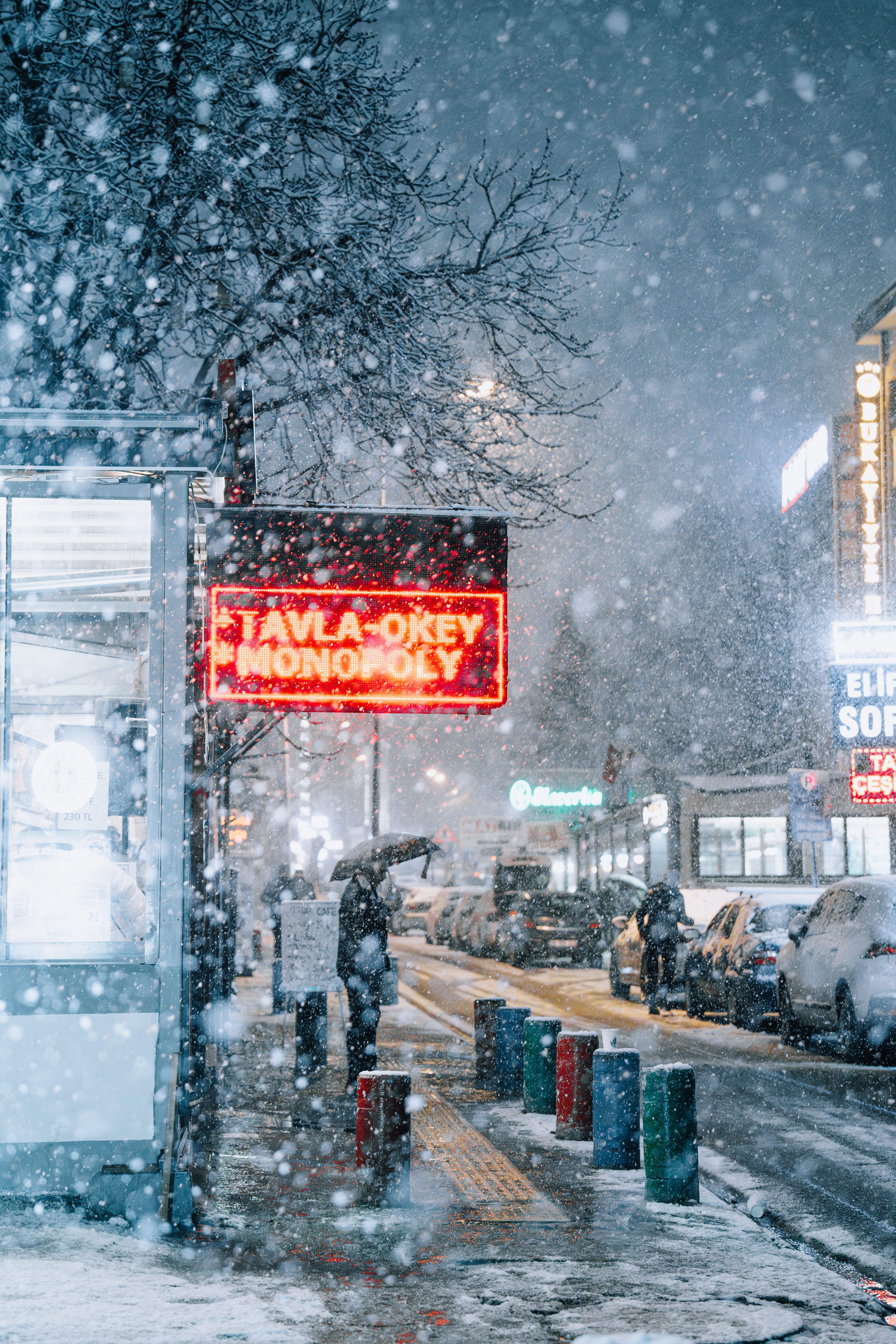 Illuminated streets of Ankara during snowfall at night with neon signs and people.