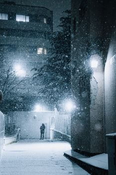 A person walks through a snowy alley in Ankara at night, illuminated by streetlights.