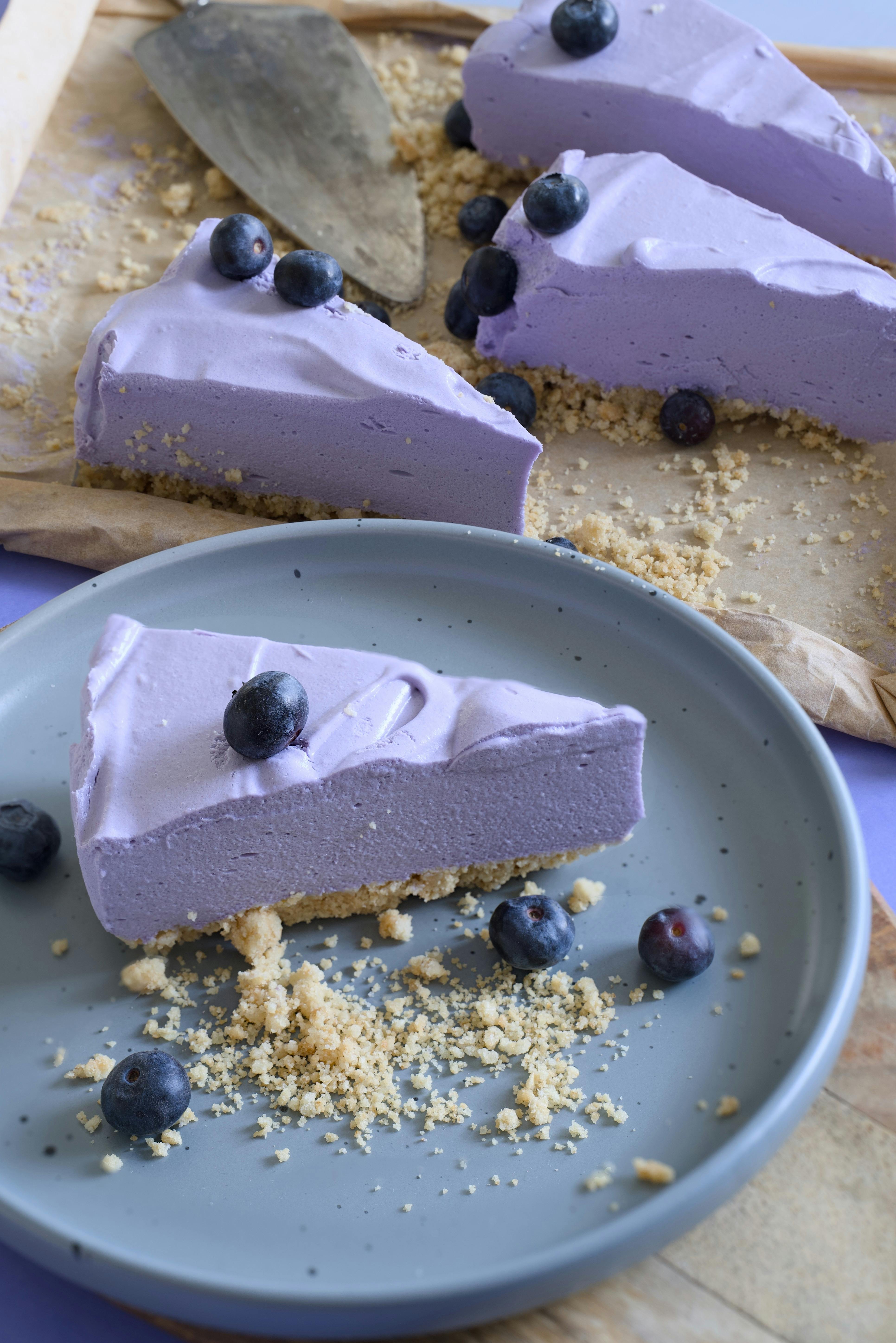 Sliced blueberry cheesecake with crumbs and fresh blueberries on a plate.