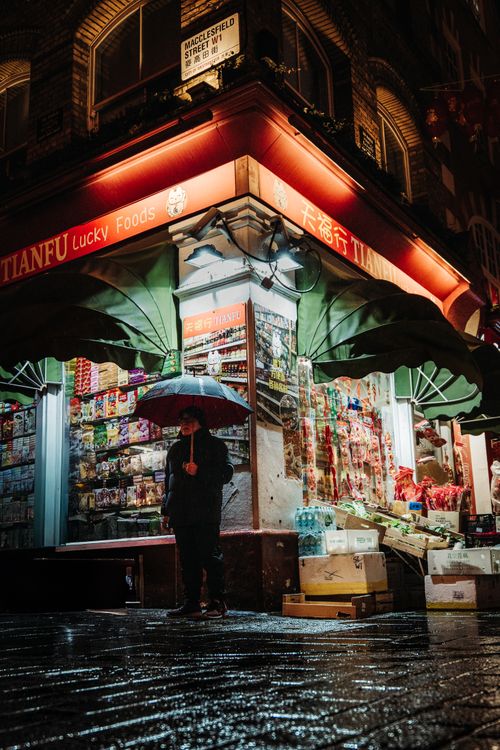 Free A nighttime street view in London's Chinatown with a person holding an umbrella near a shop. Stock Photo