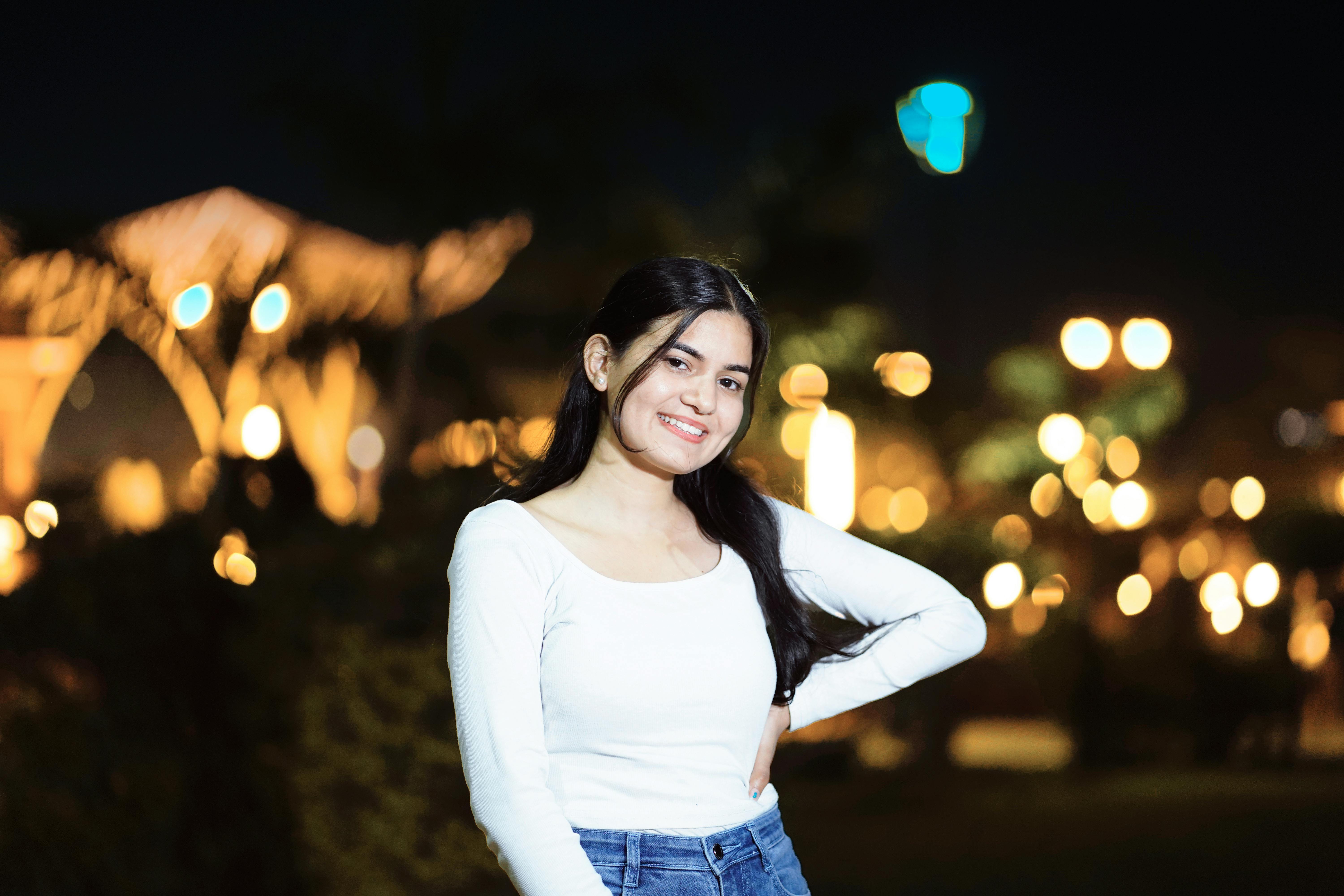 Smiling woman poses in a nighttime cityscape with blurred lights.