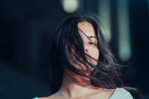 Free Close-up portrait of a woman with dramatic lighting and hair blowing across her face. Stock Photo
