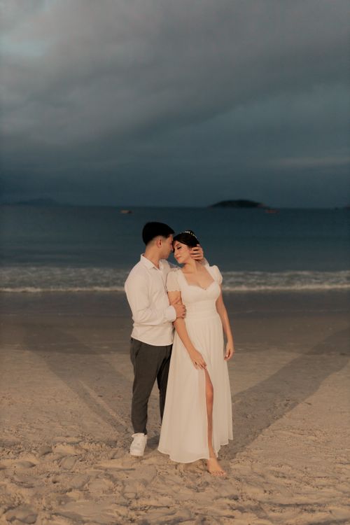 Free A couple in love embracing on a sandy beach during twilight, with a dramatic sky overhead. Stock Photo