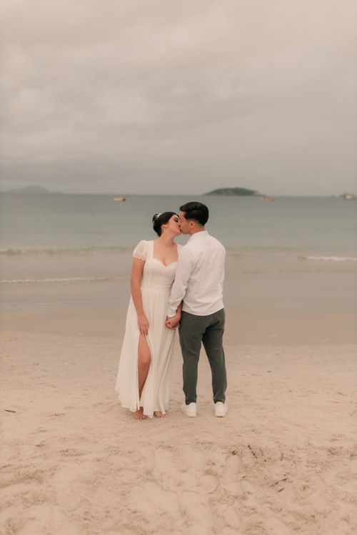Free A loving couple kissing on a serene beach at sunset, creating a romantic scene. Stock Photo