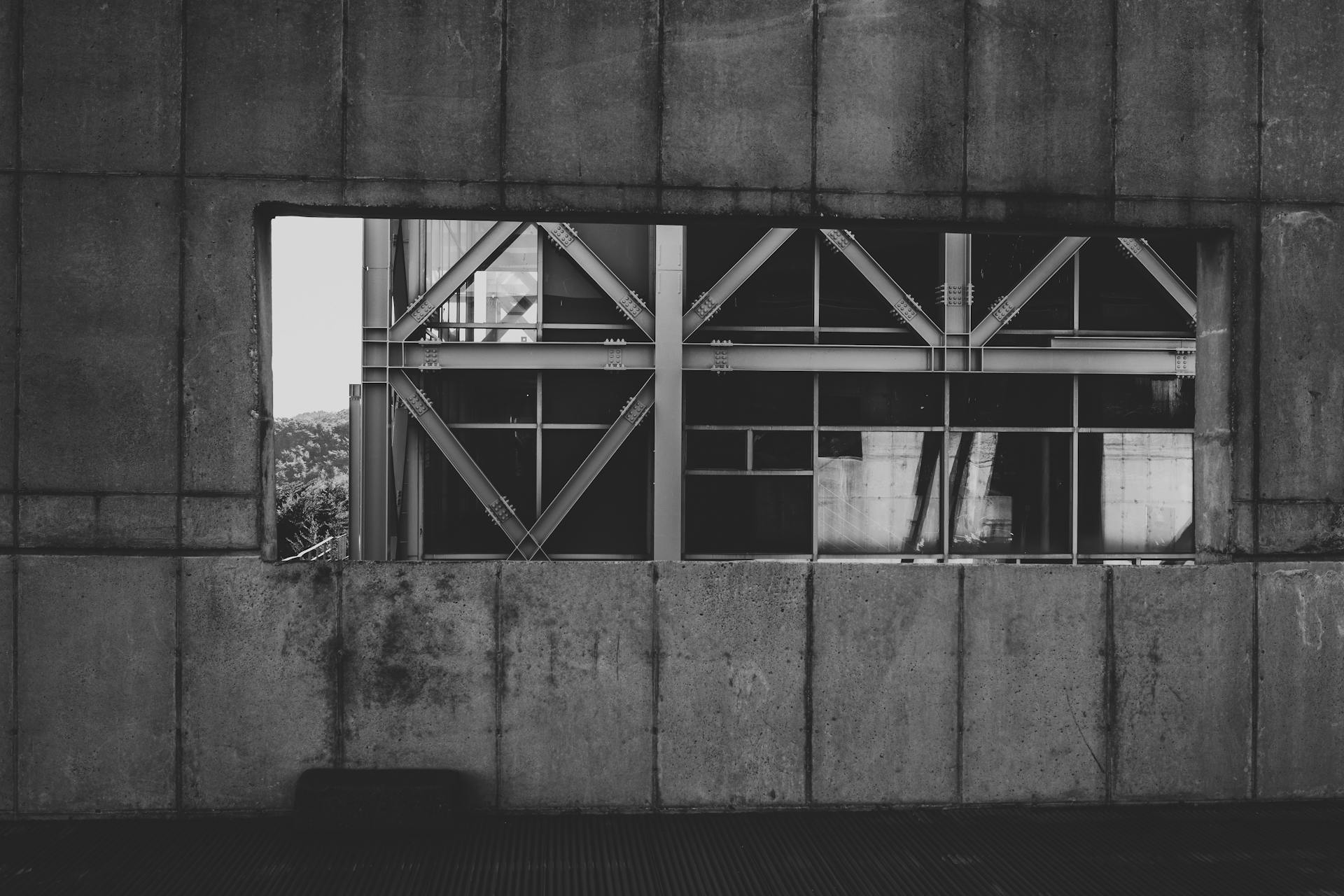 Black and white photo of modern structural beams visible through a concrete wall.