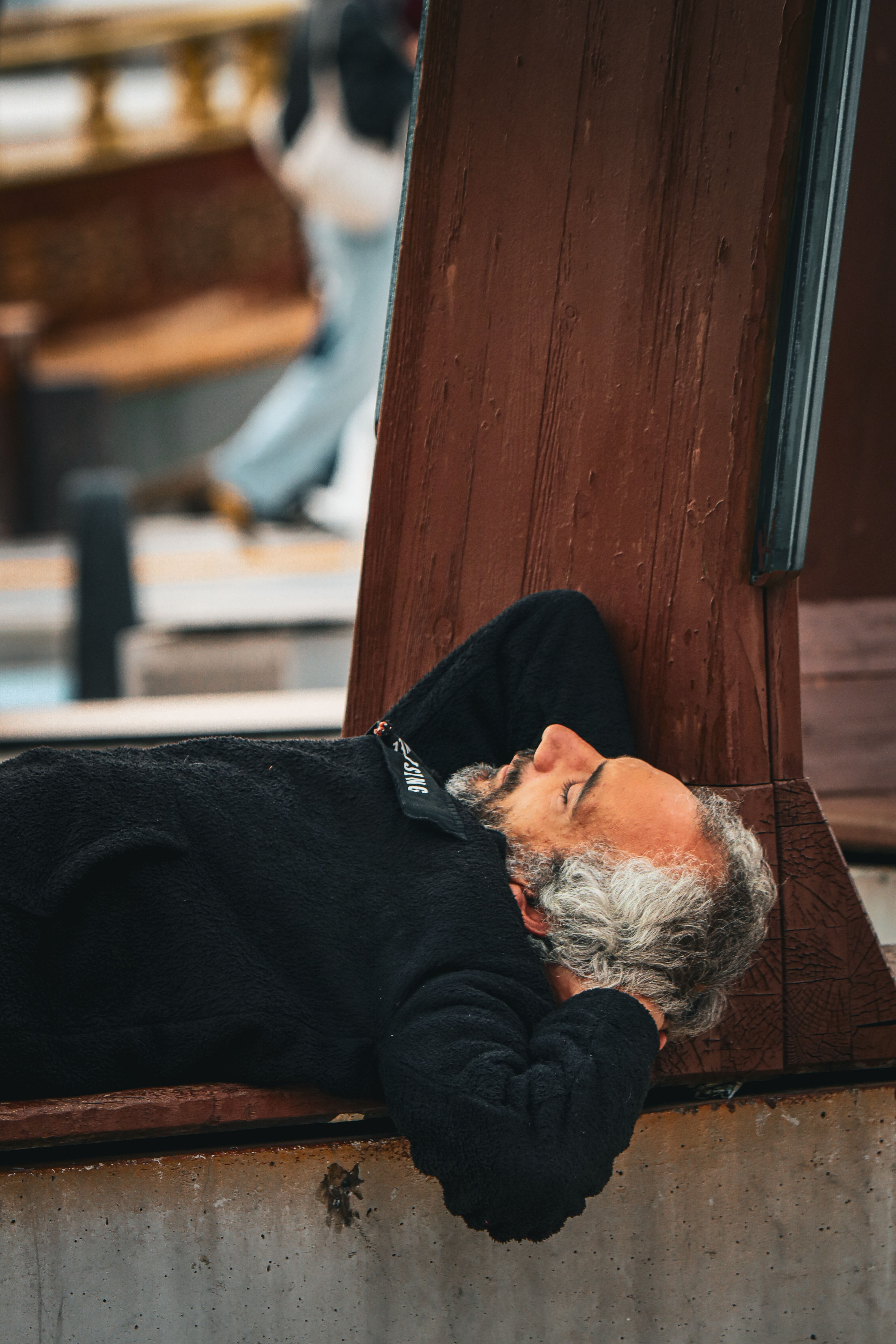 Seated Man Resting Against a Wooden Structure · Free Stock Photo