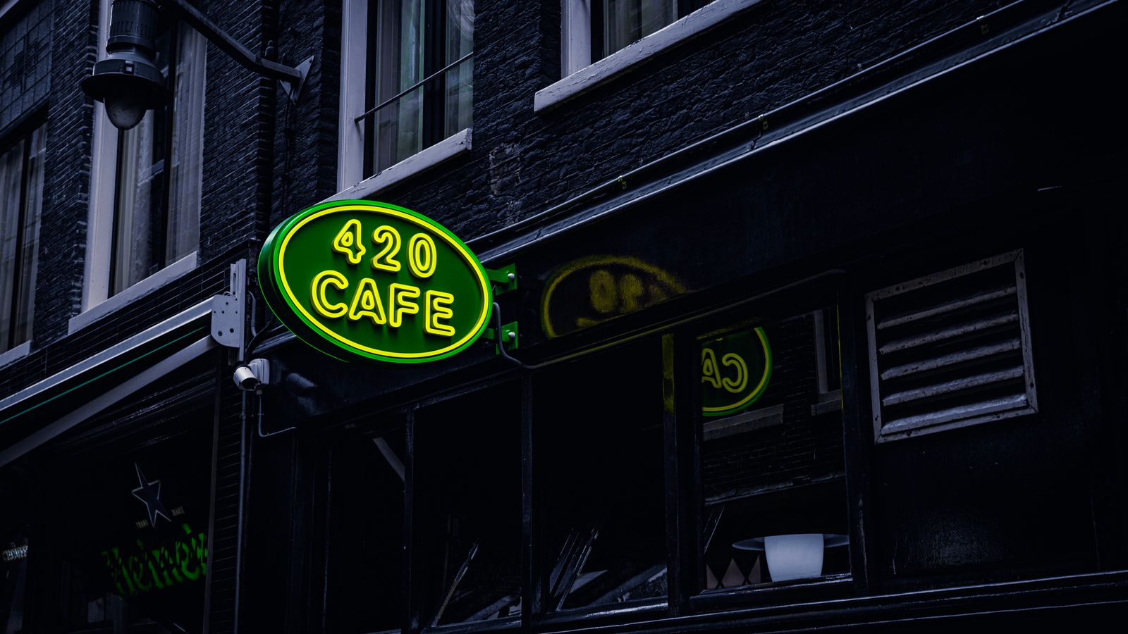 Green neon sign '420 Cafe' on a building facade in Amsterdam, creating a vibrant city atmosphere.