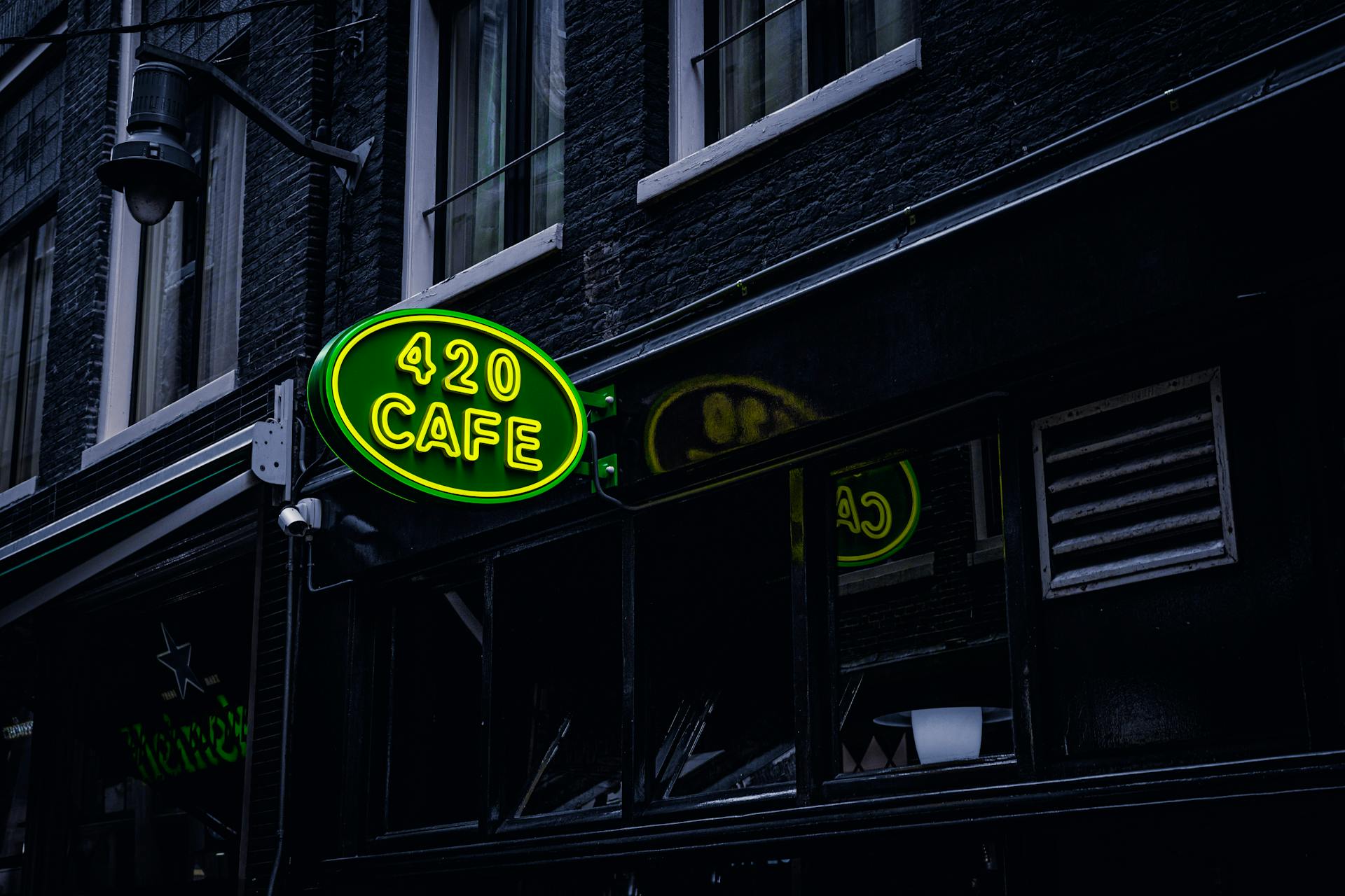 Green neon sign '420 Cafe' on a building facade in Amsterdam, creating a vibrant city atmosphere.