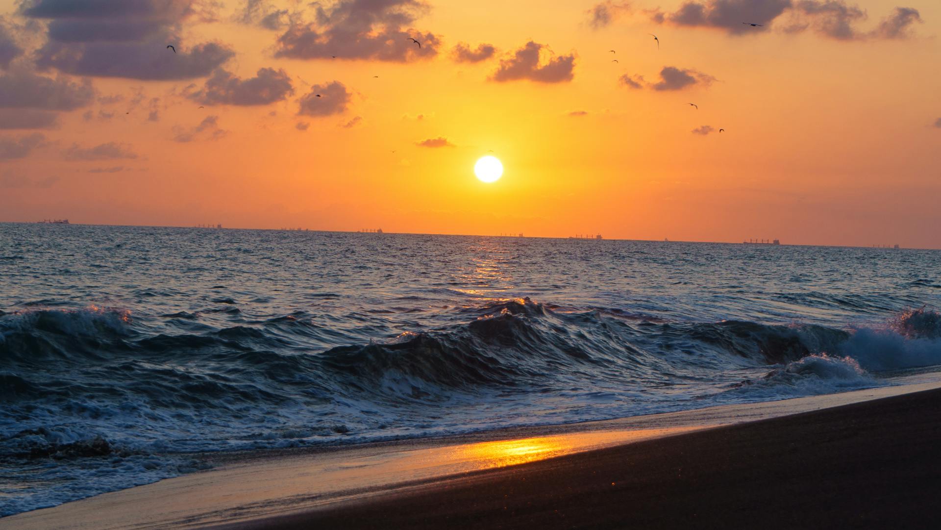 Breathtaking sunset over ocean with waves crashing on the shore.