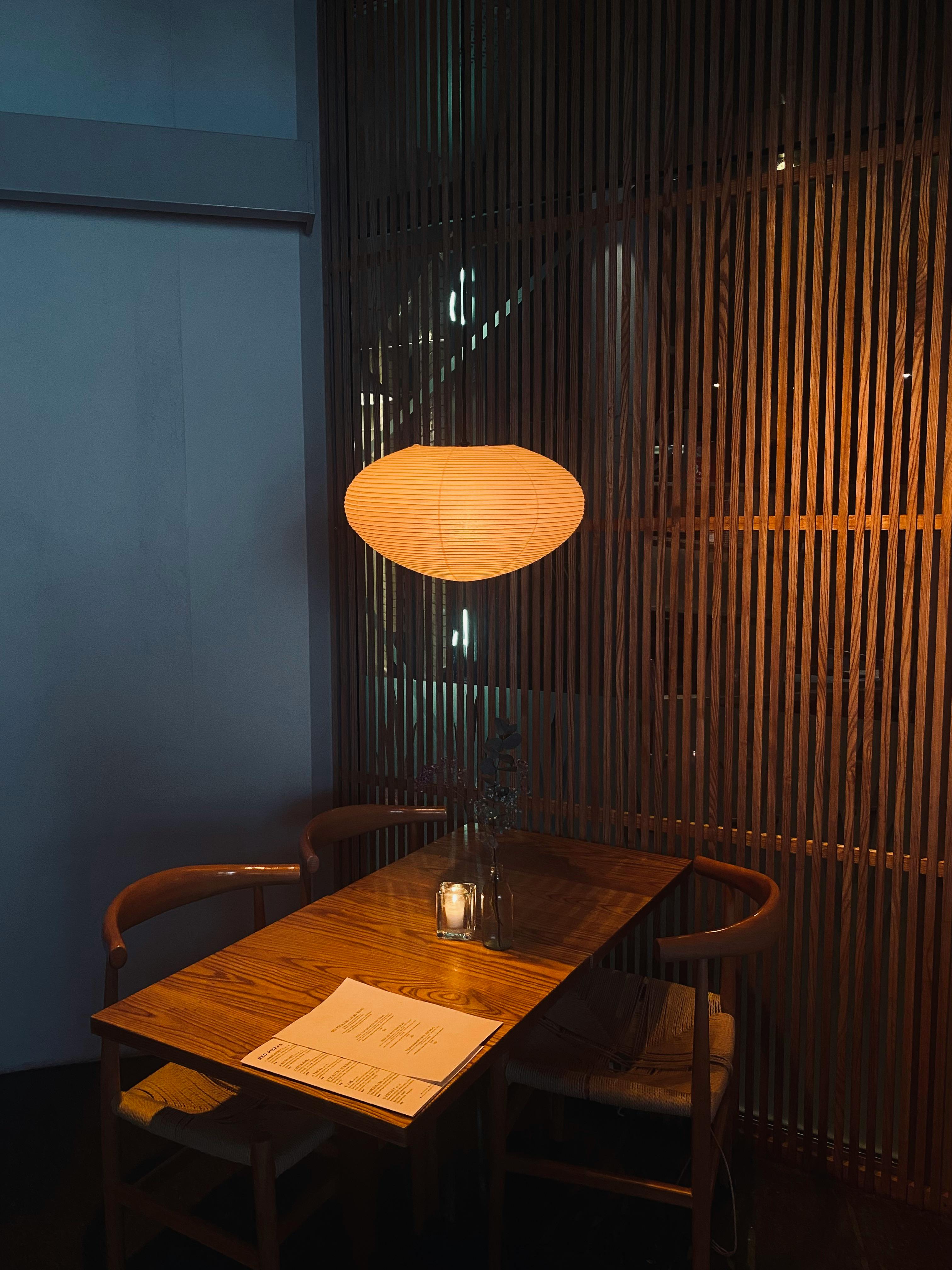 Warm, intimate dining setup with a glowing lampshade over a wooden table and chairs.