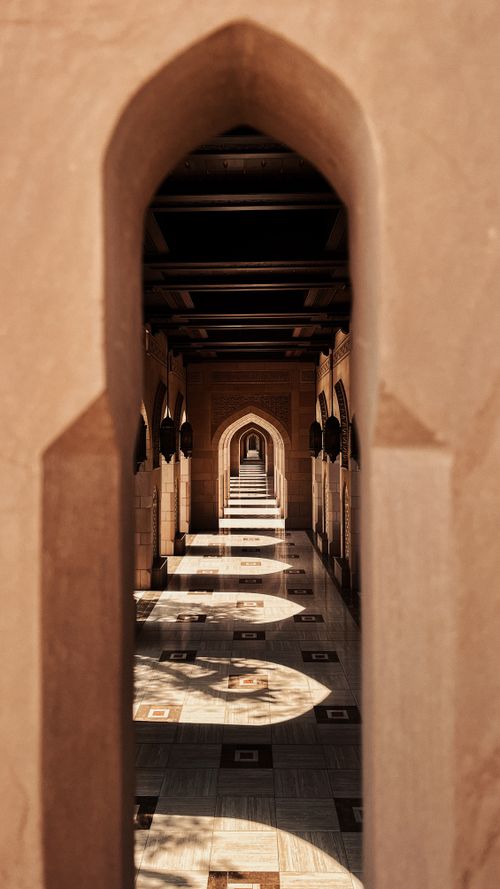 Free Sunlight casts patterns through arched hallway in Omani architecture, showcasing intricate design. Stock Photo