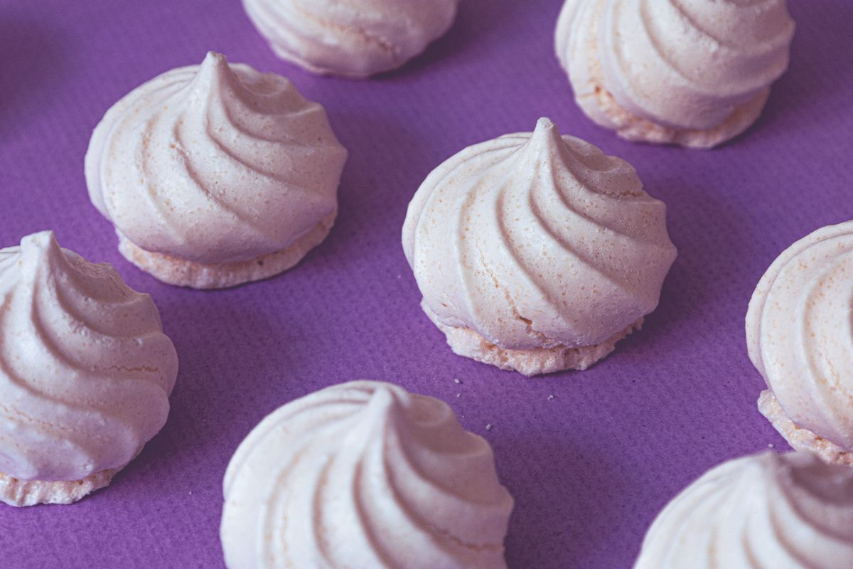 Delicate artisan meringue cookies arranged on a vibrant purple surface, capturing a sweet dessert charm.
