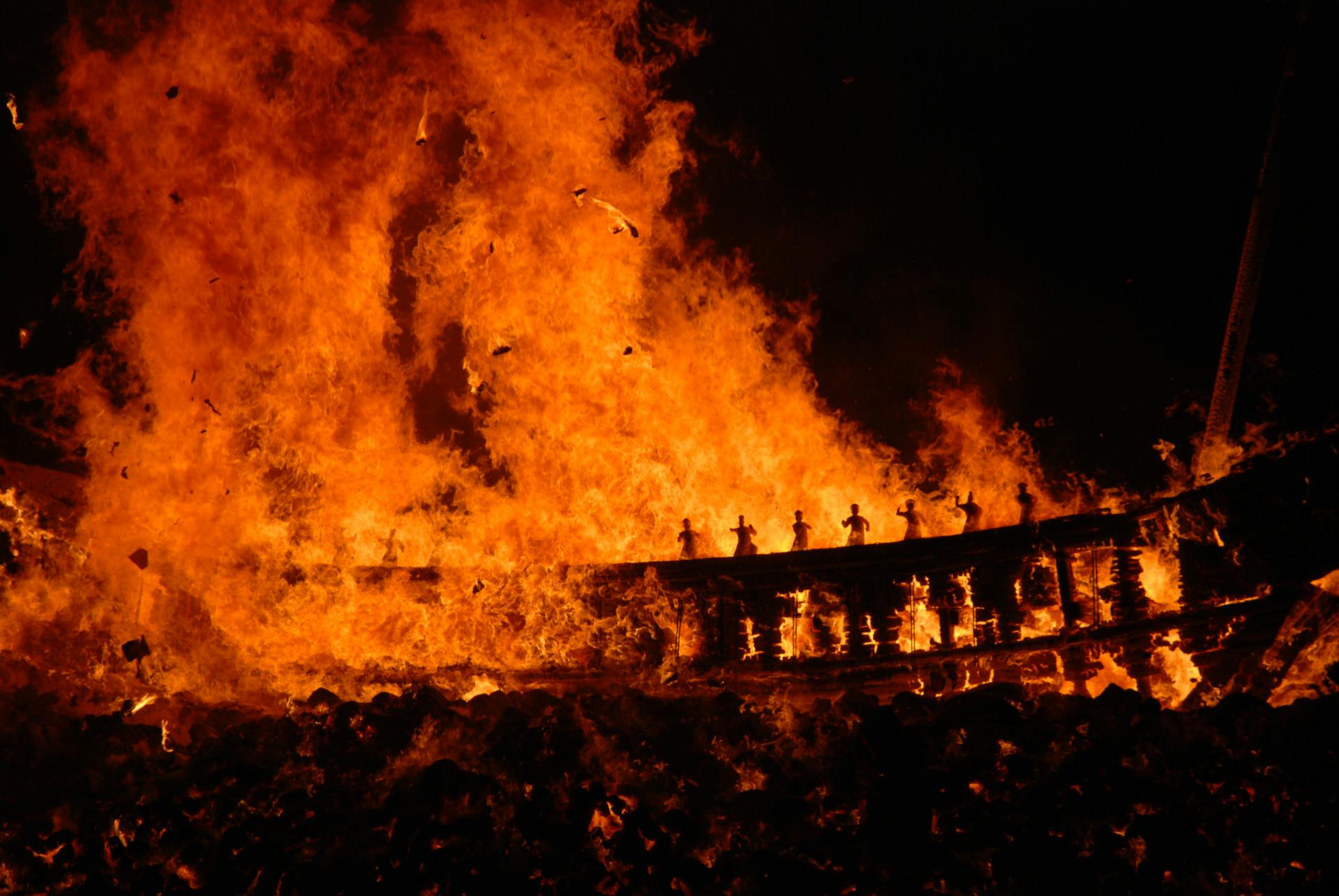 A dramatic scene of a Viking ship burning in a festival setting, vivid flames illuminate the night.