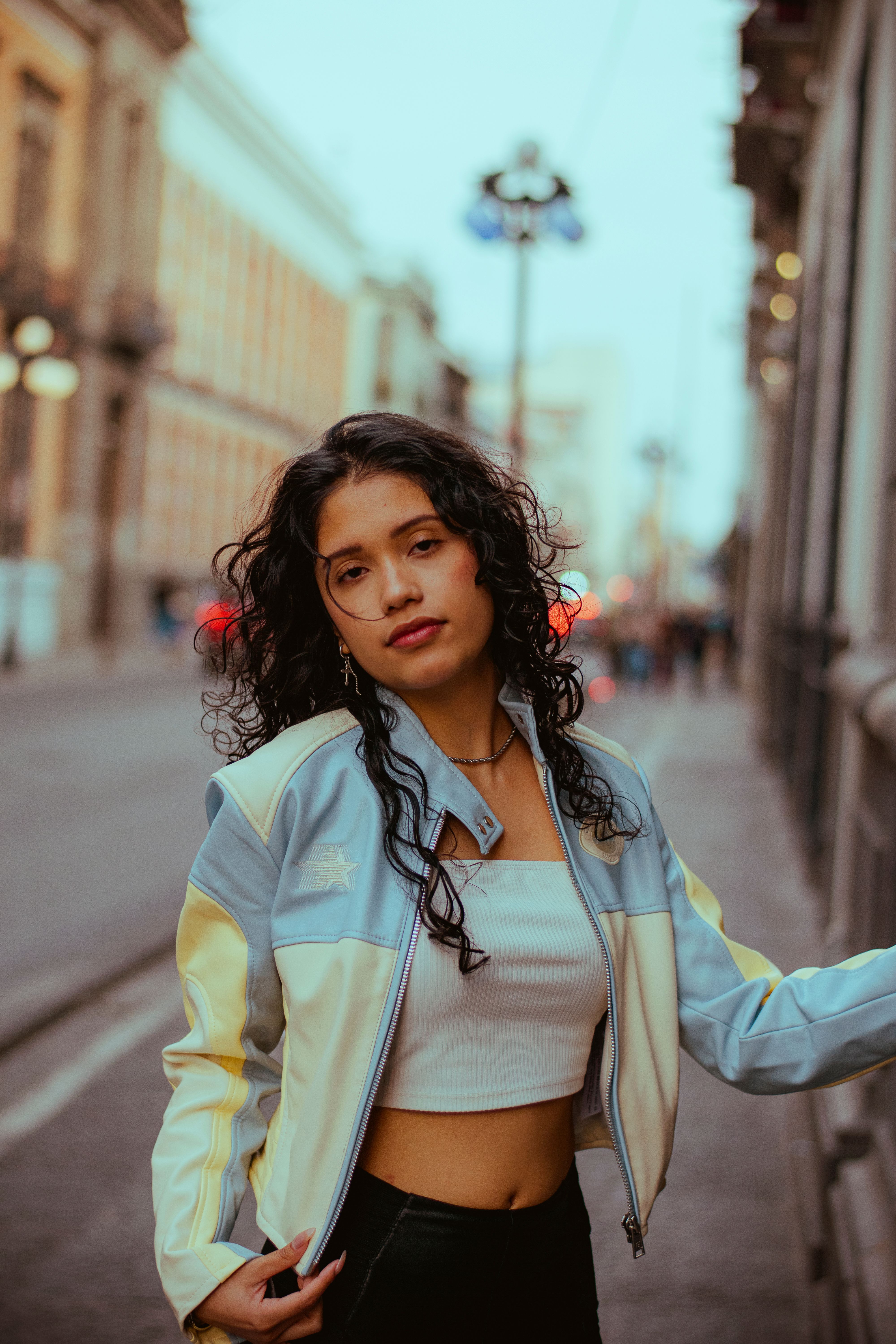 Stylish young woman in urban setting wearing pastel jacket and white crop top.
