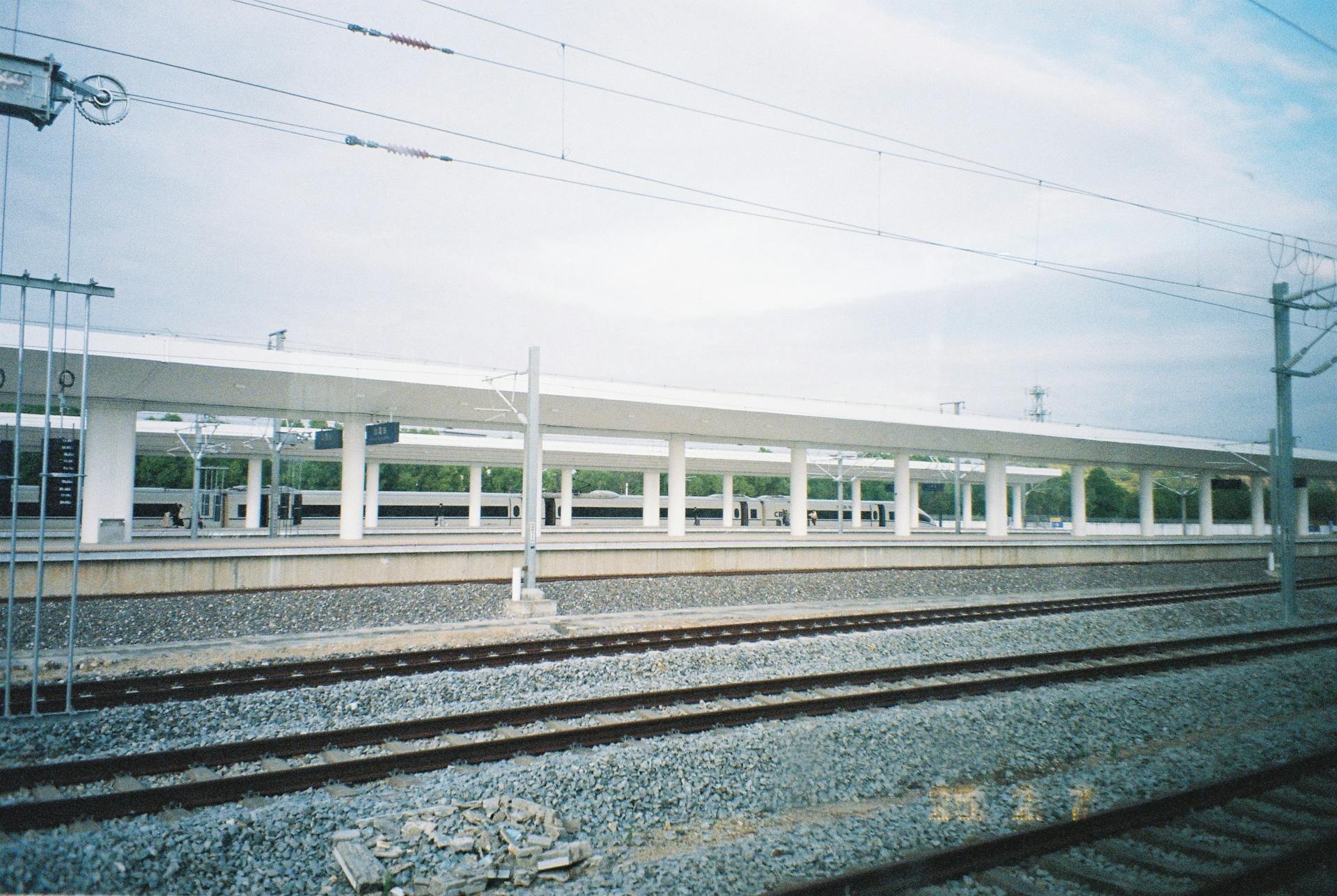 Wide view of an empty train station platform featuring multiple tracks and overhead electric lines.