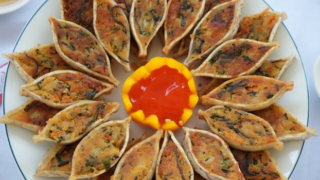 A plate of vegan dumplings arranged with sweet chili sauce in a bell pepper bowl.