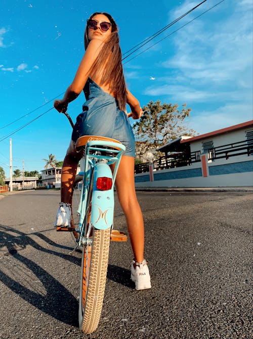 Back View Photo of Woman in Blue Dress and Sunglasses Sitting on Blue Bicycle Looking Back