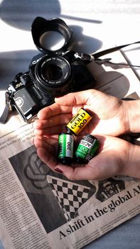 Hands holding film rolls near a vintage camera on a newspaper.