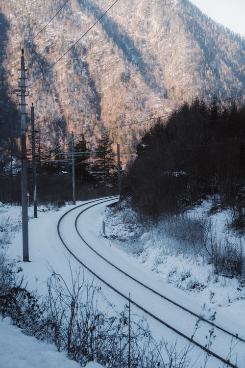 Free Serene winter railway winding through snow-covered mountains, creating a picturesque travel scene. Stock Photo