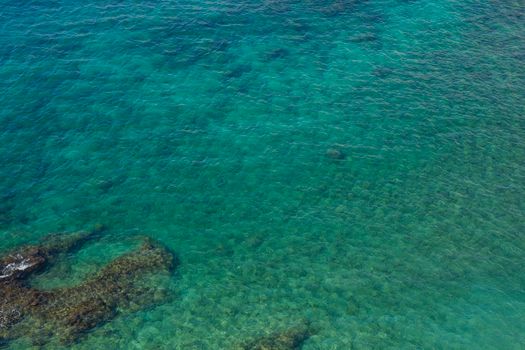 A calming aerial view of clear turquoise ocean waters showing underwater rock formations.