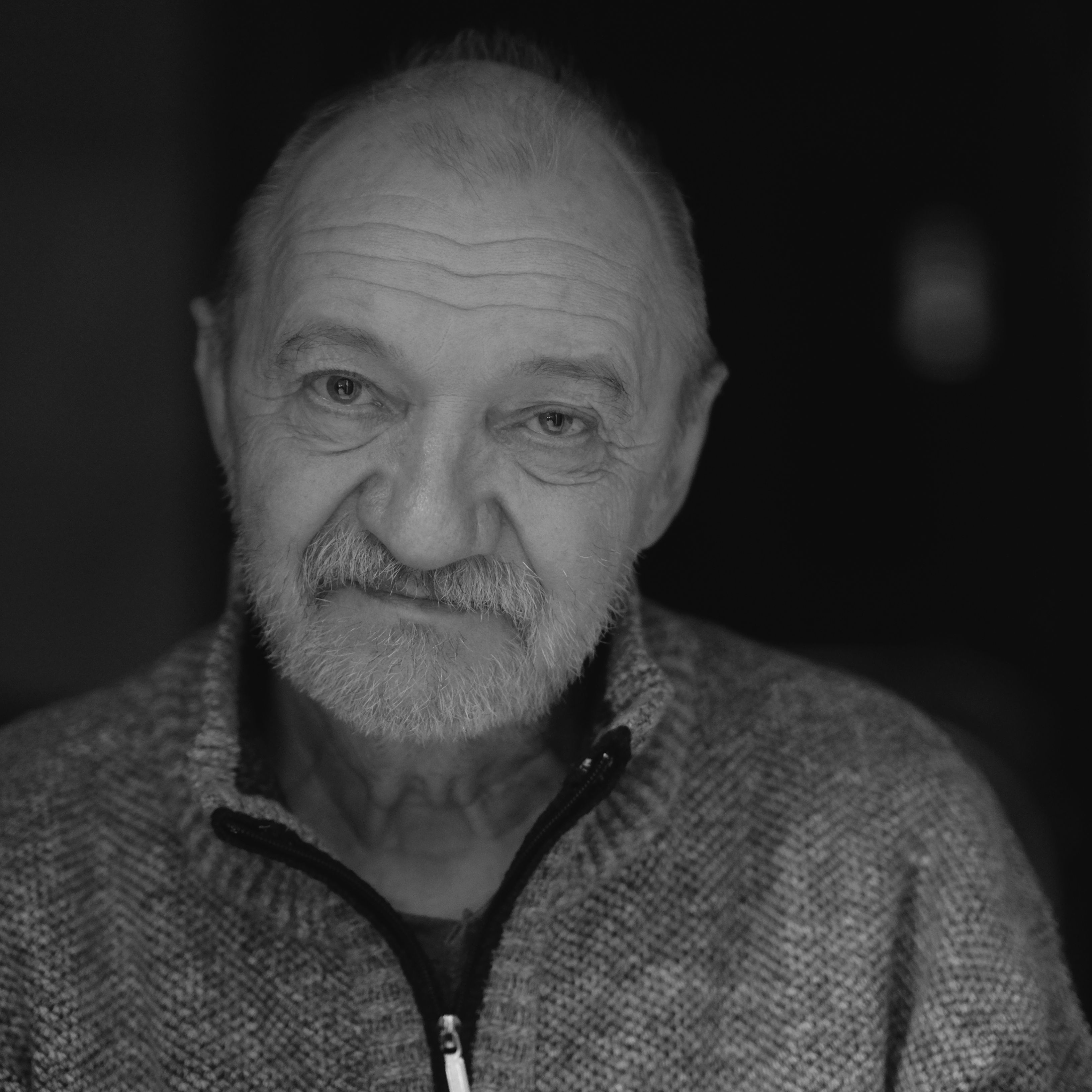 Black and white portrait of an elderly man with a warm expression wearing a cozy sweater.
