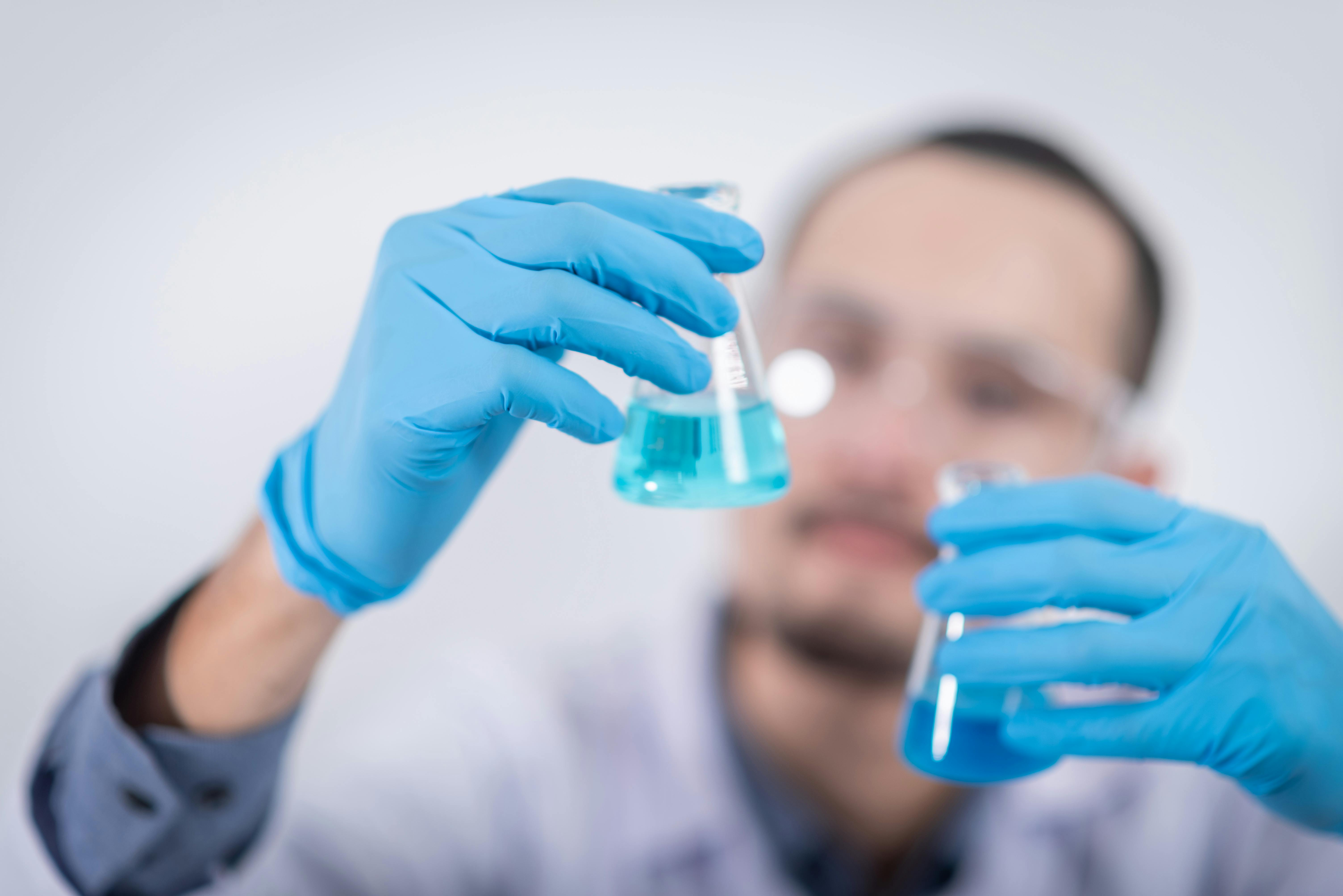 Scientist holding two flasks, each containing blue liquid.