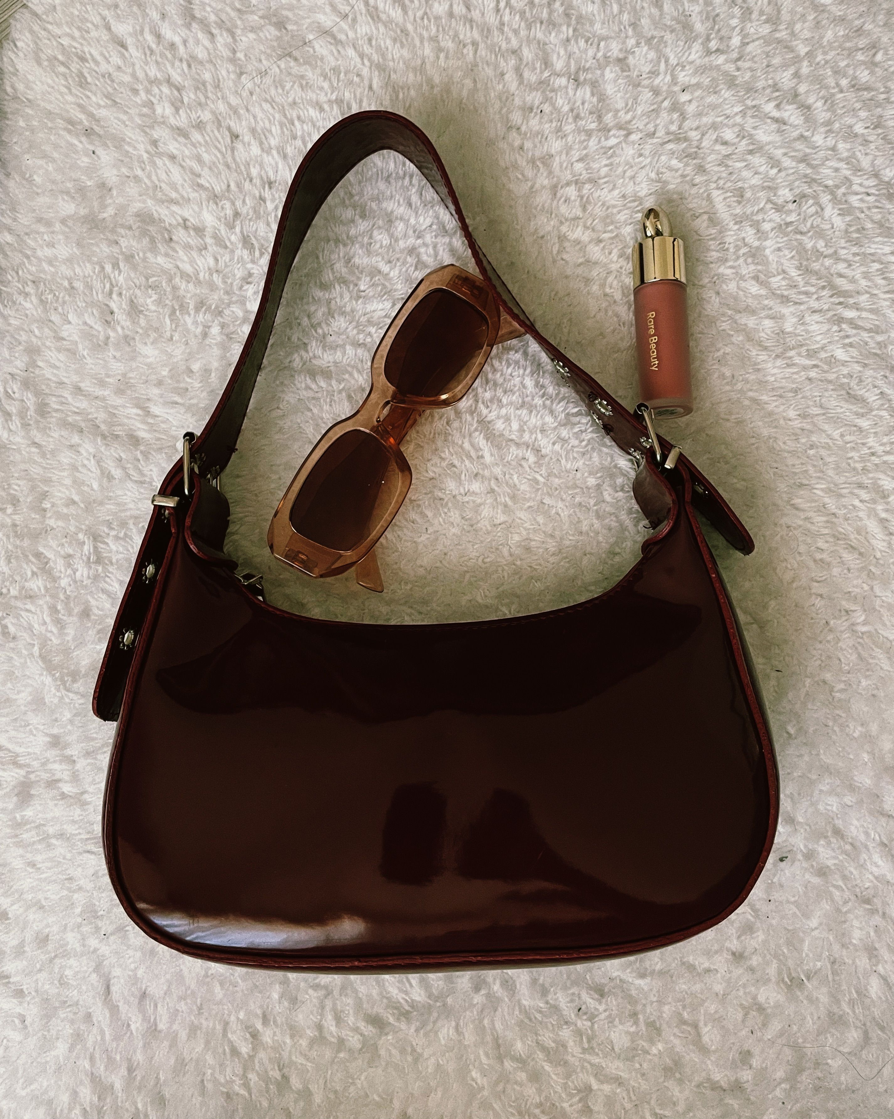 Elegante bolsa marrom acompanhada de óculos de sol e batom sobre superfície texturizada.
