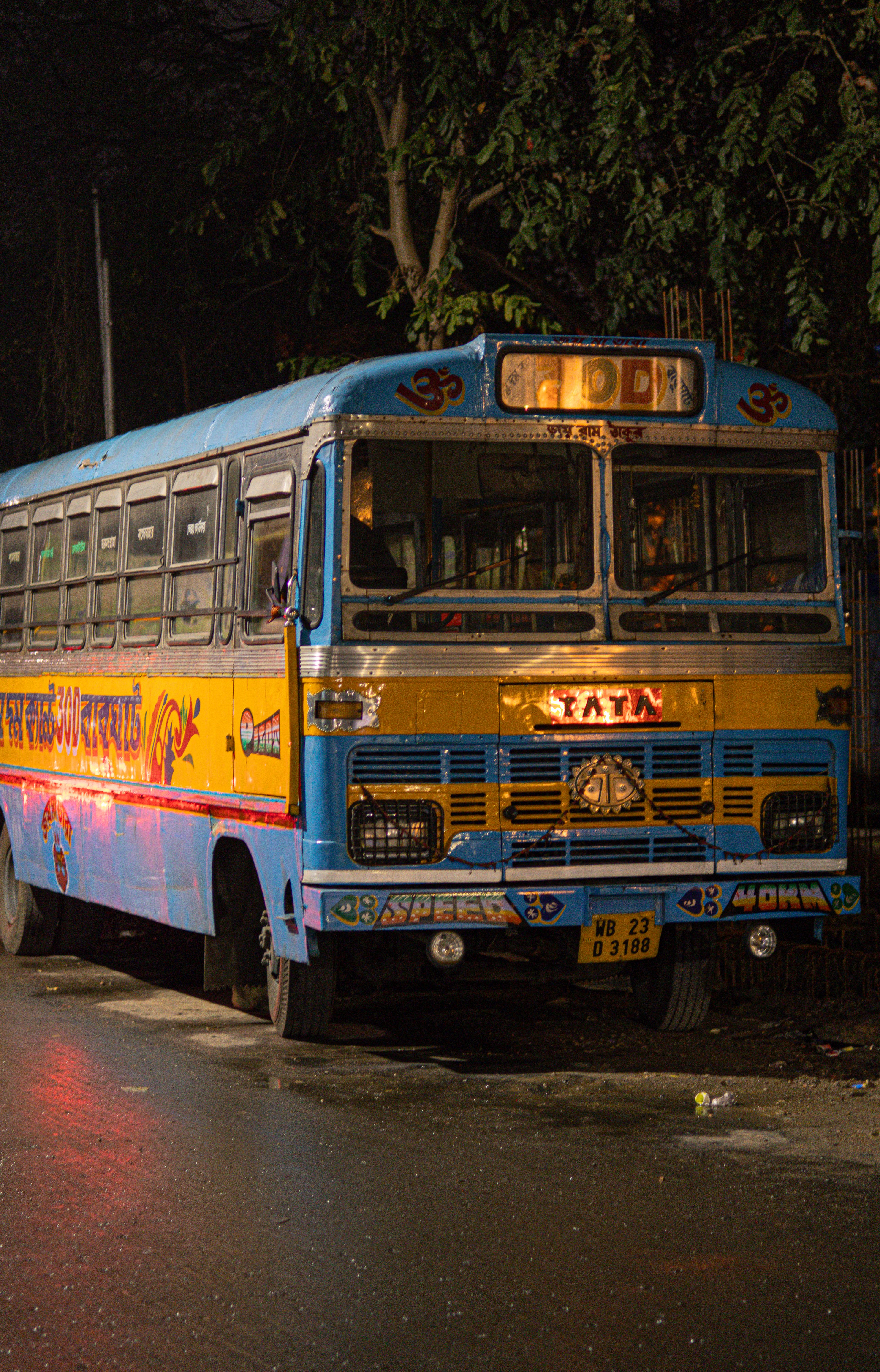 Vibrant Tata bus parked on a wet street at night, emitting a warm glow.