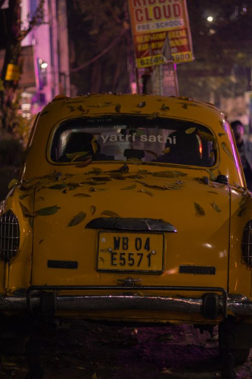 Free Yellow taxi covered in leaves parked on a city street at night, Kolkata. Stock Photo