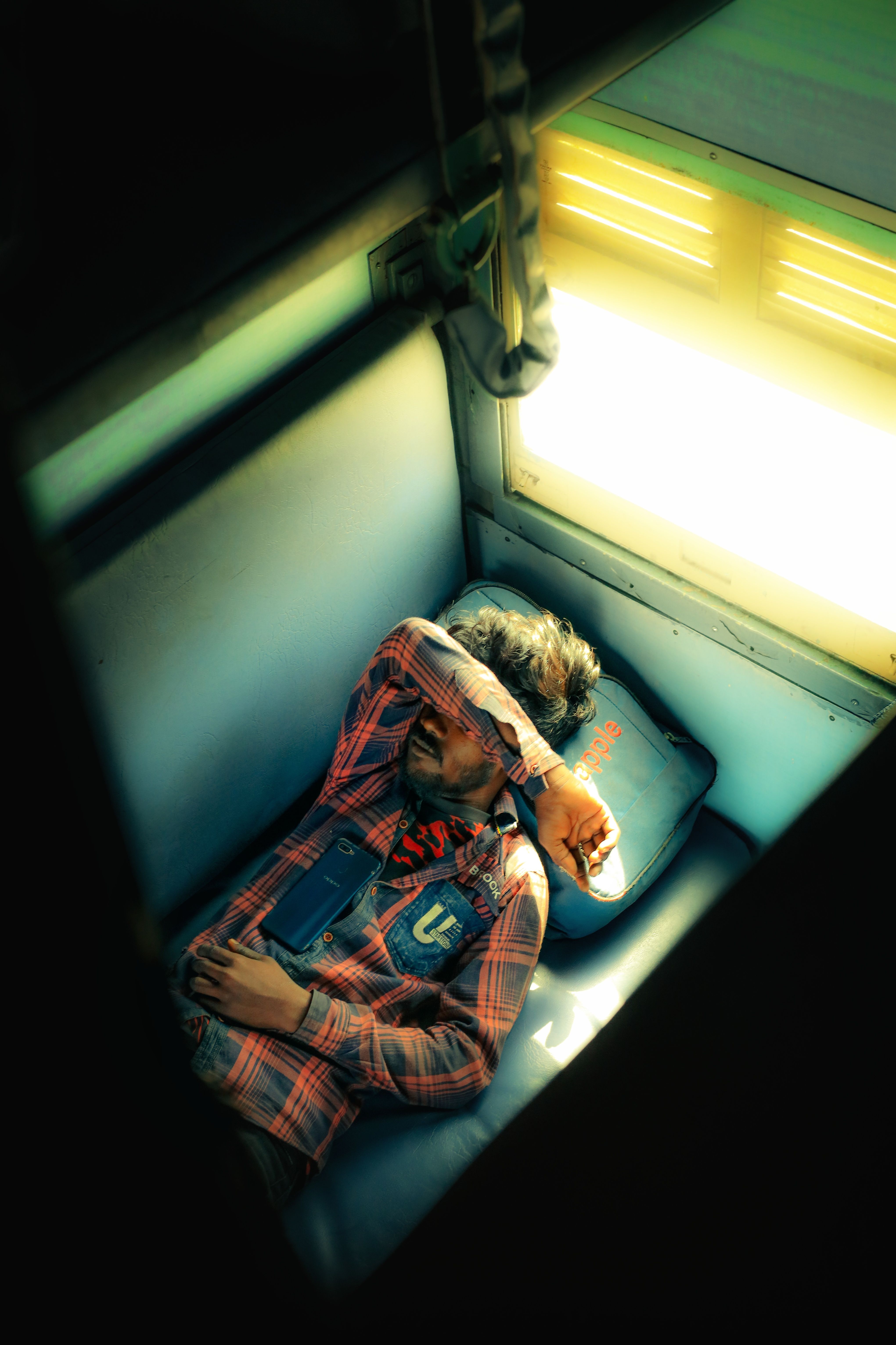 A man sleeping in a train compartment during the day, sunlight filtering in.