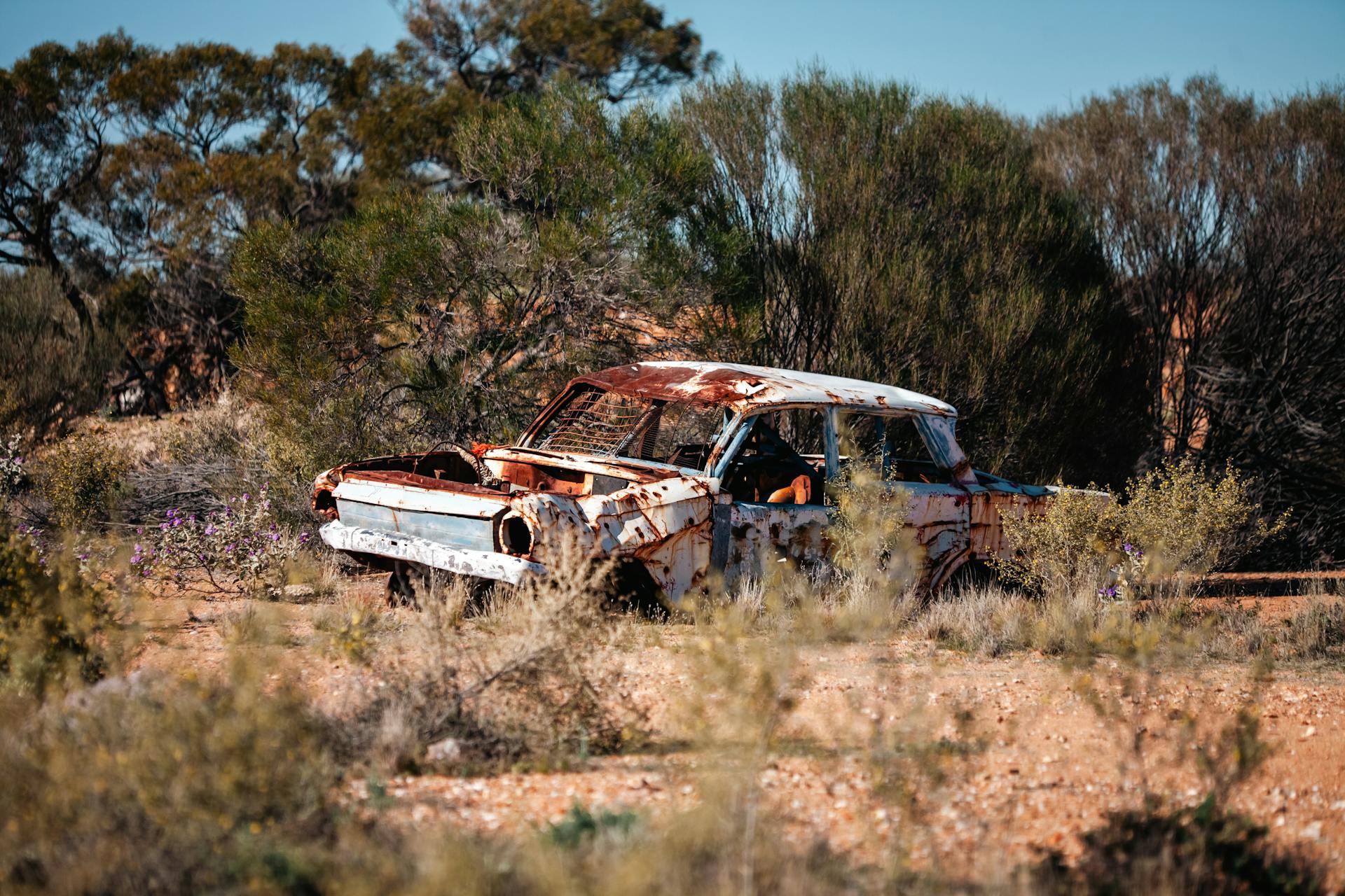 A weathered, rusted car is abandoned in the bushland of Laverton, Western Australia.