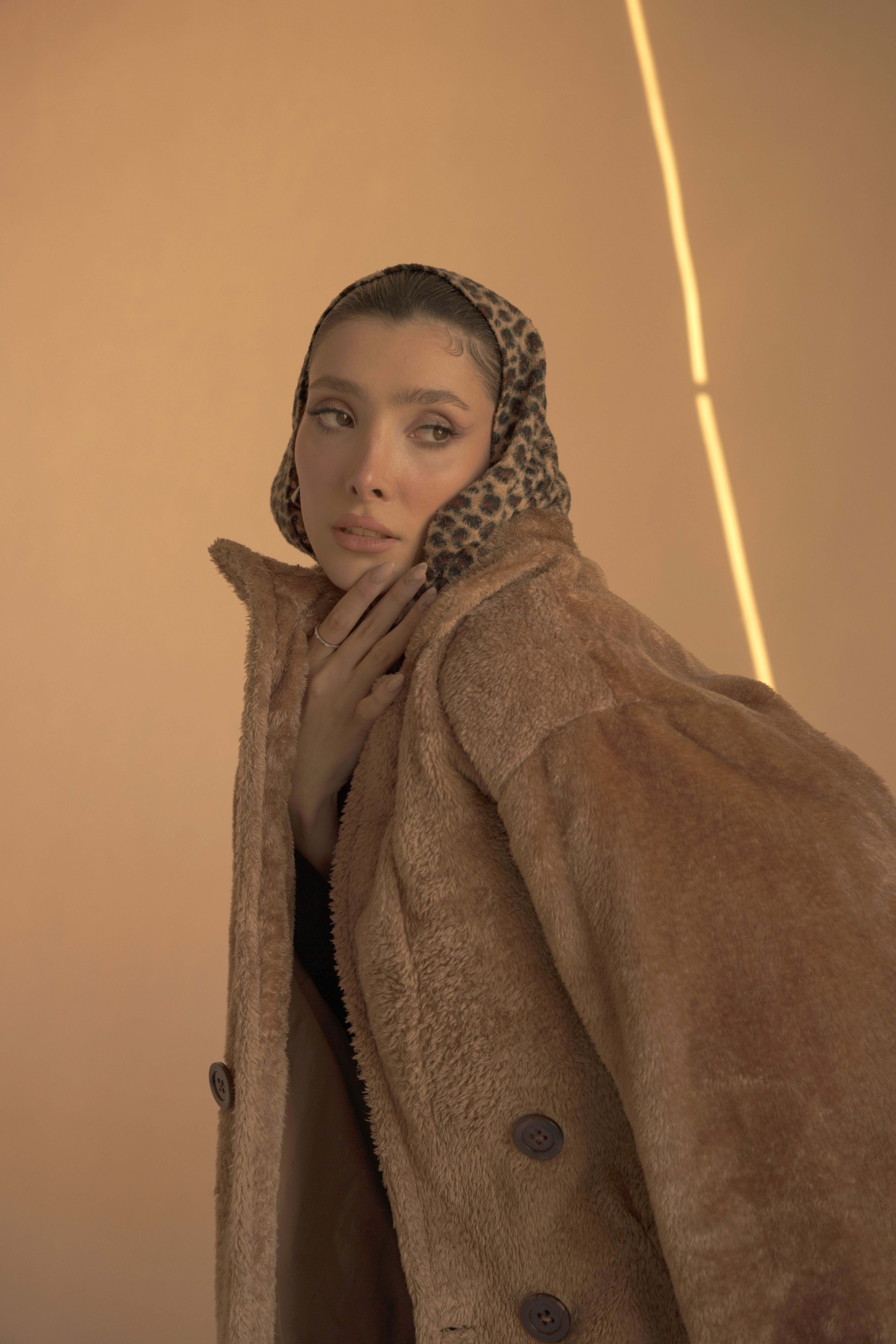Elegant woman in fur coat and leopard print scarf in warm lighting for a fashion shoot.