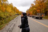 一位女士在风景秀丽的秋日道路上，用相机捕捉充满活力的树叶和车流景象