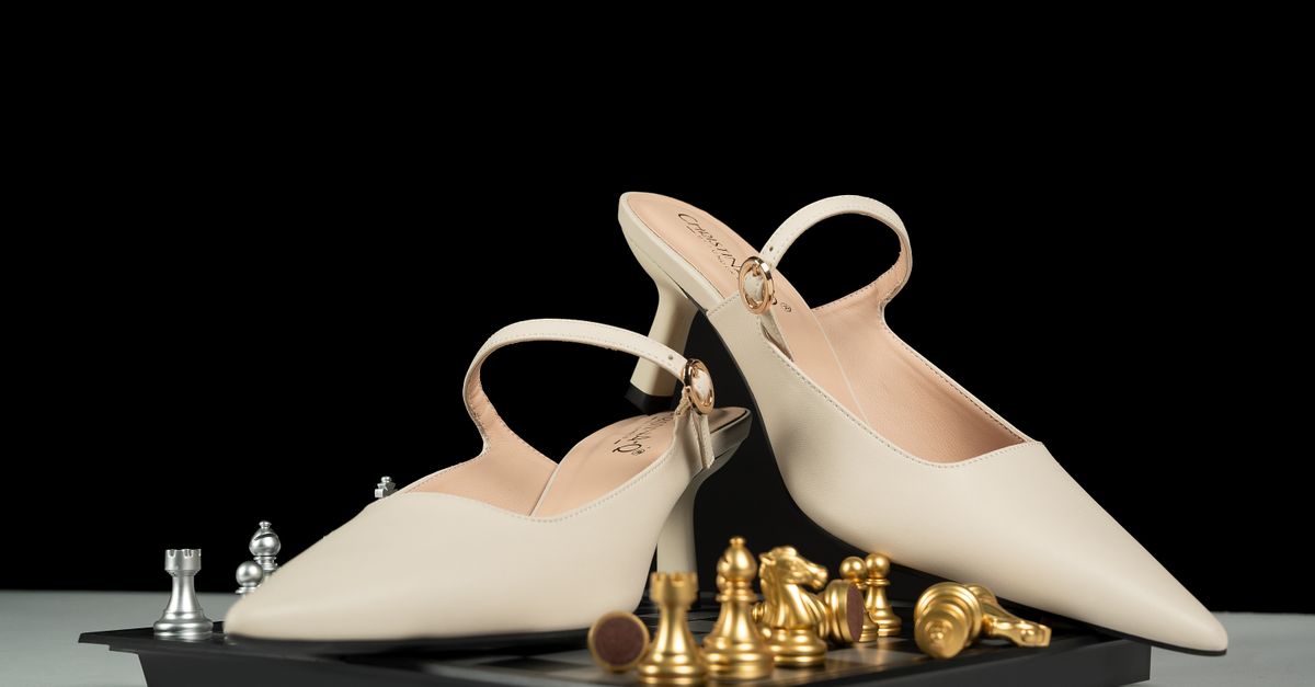 Chic beige high-heeled shoes elegantly placed on a chessboard with golden pieces, perfect for fashion concepts.