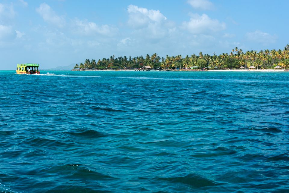Colorful tour boat cruising past a palm-covered island with thatched huts on shore