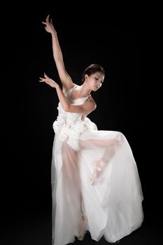 Graceful ballet dancer in a flowing white dress executing an artistic pose on a dark background.